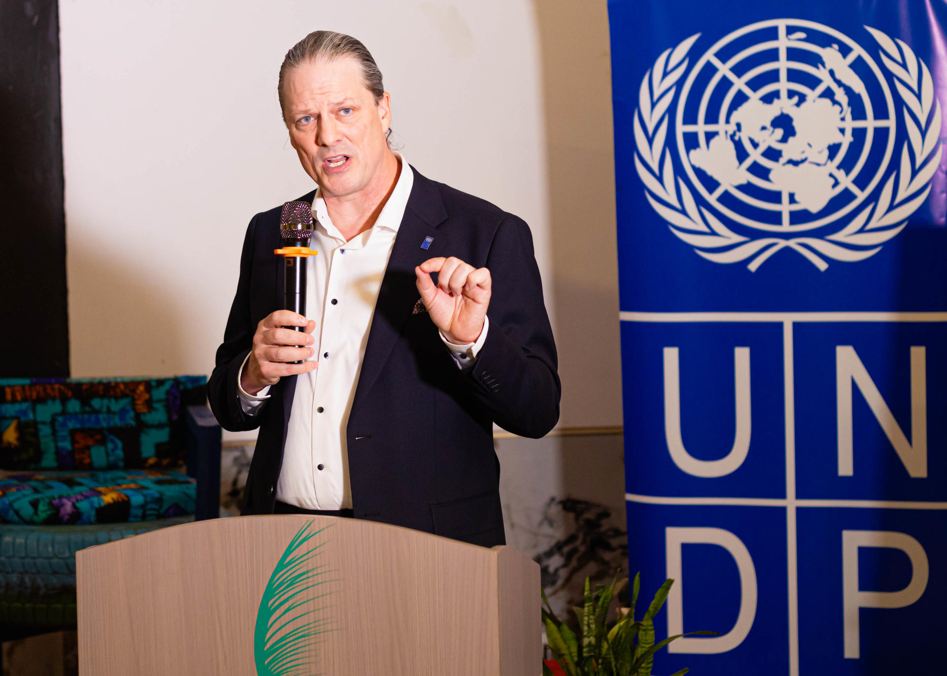 Speaker at podium in a suit with UNDP banner behind and a microphone.