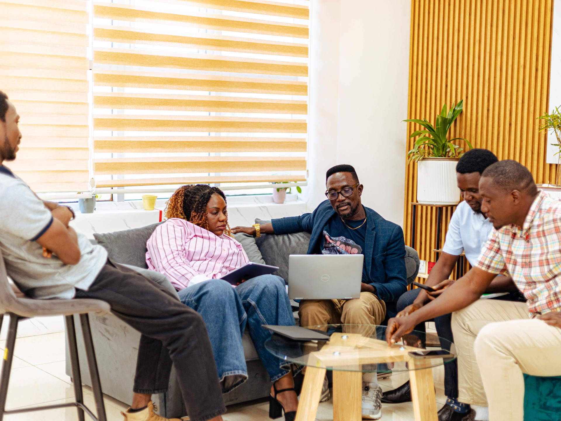 Diverse group of adults sitting in a circle, with a laptop on a coffee table in a bright room.