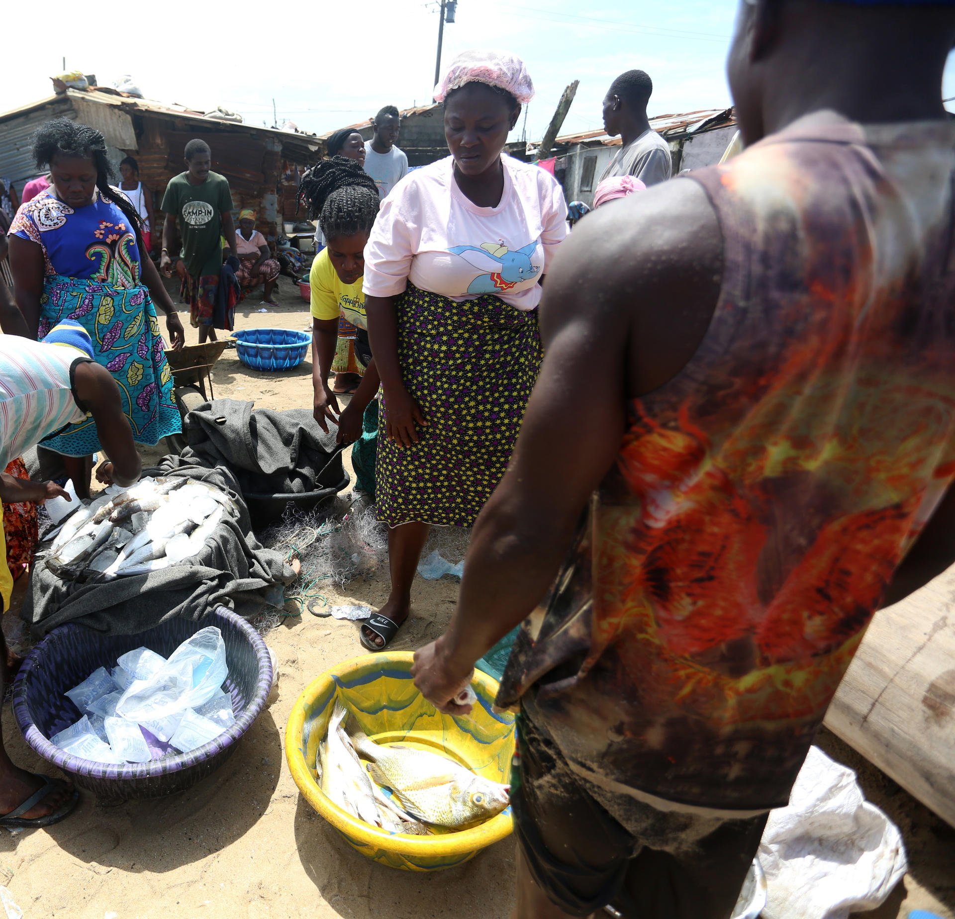 Busy outdoor market with people gathered around blue and yellow tubs of fish.