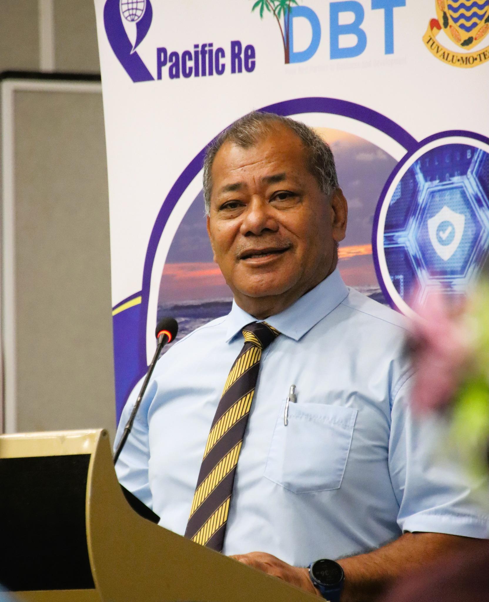 Man in light blue shirt and striped tie giving a presentation at a podium with a banner backdrop.