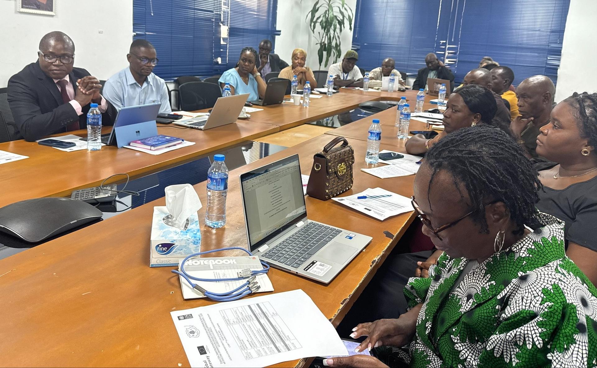 Photo of professionals in a conference room around a long table with laptops and documents.