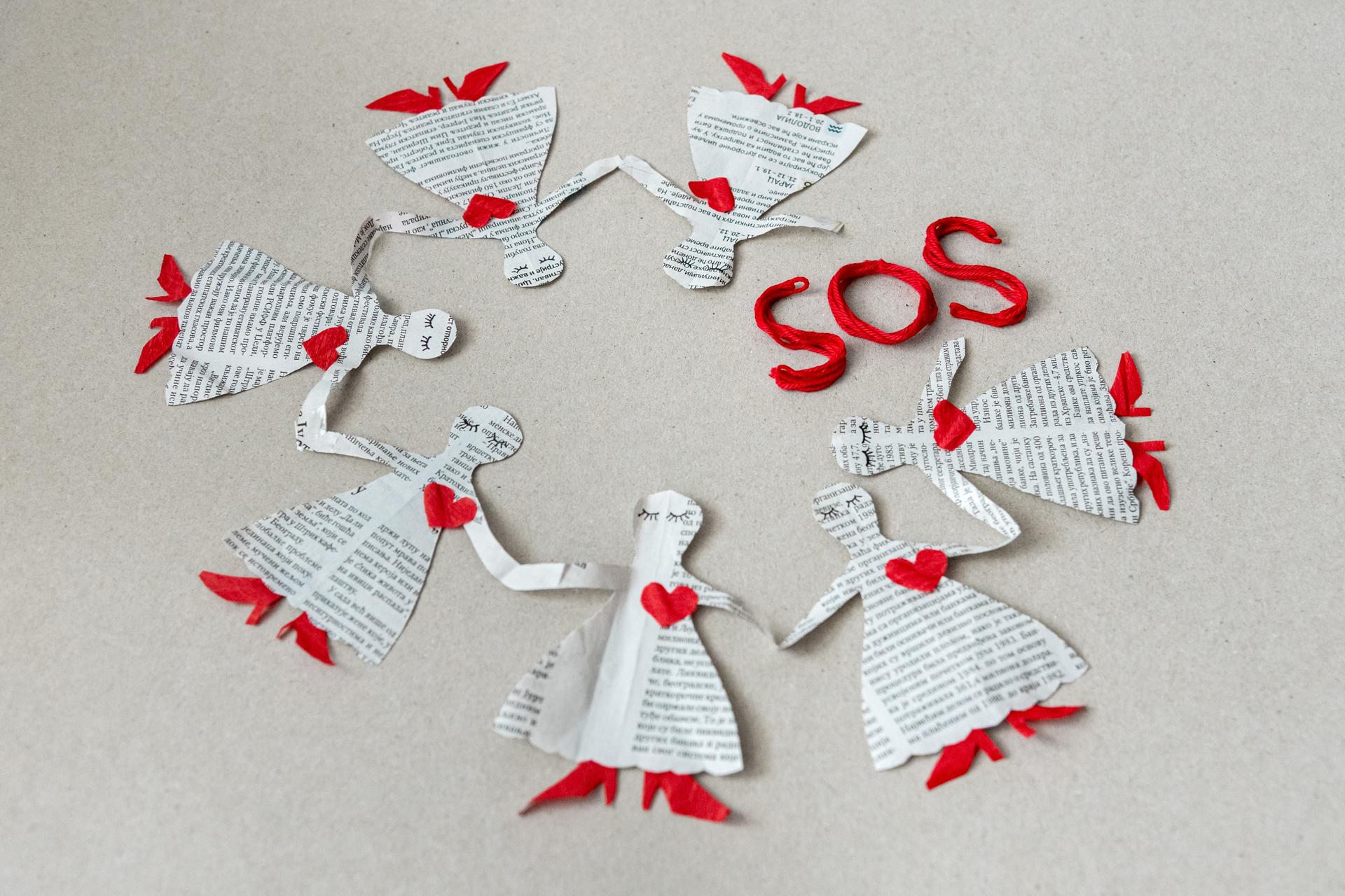 Paper dolls in white dresses with red trim arranged in a circle, with SOS letters.