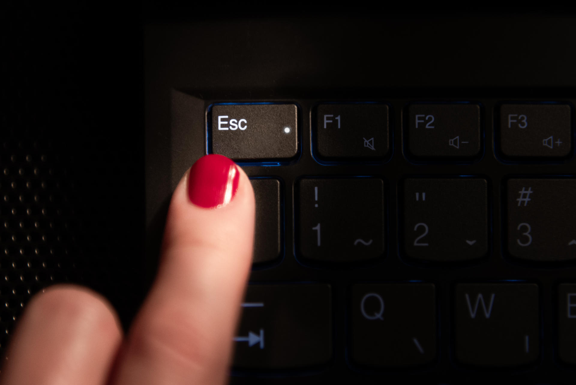 Close-up of a finger with a red nail pressing the Esc key on a dark laptop keyboard.