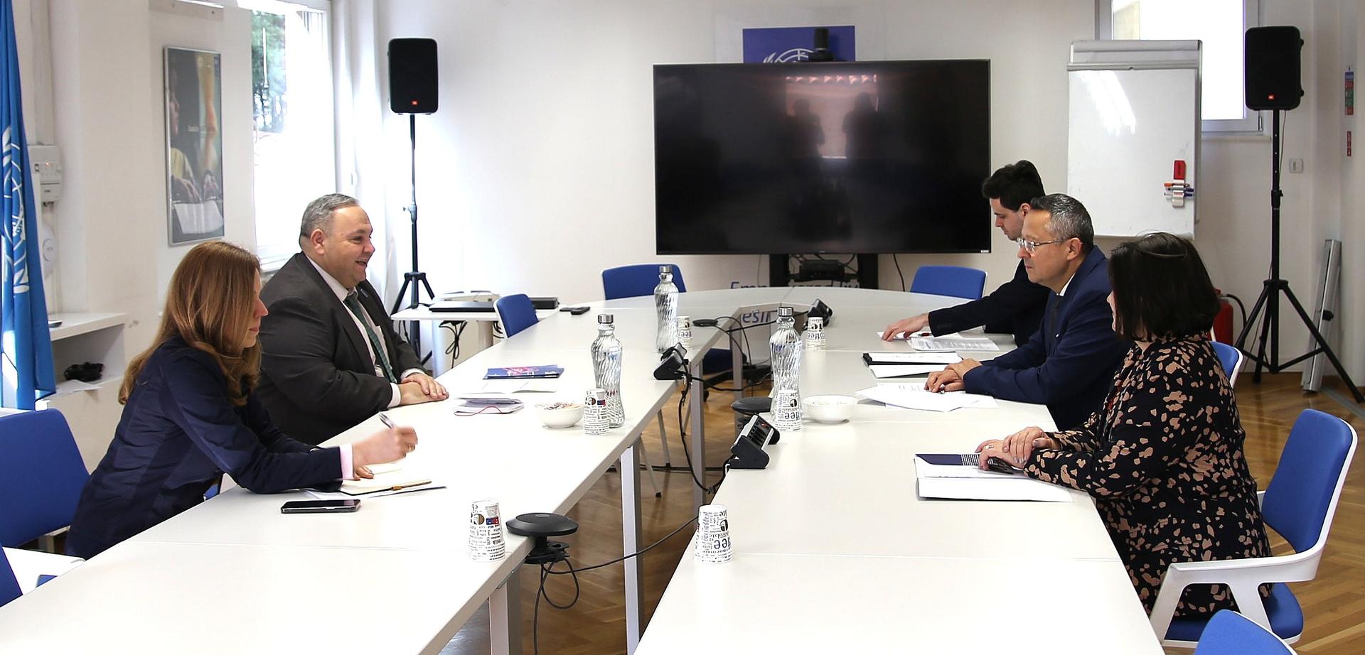 Group of professionals seated around a conference table in a meeting room with a large screen.
