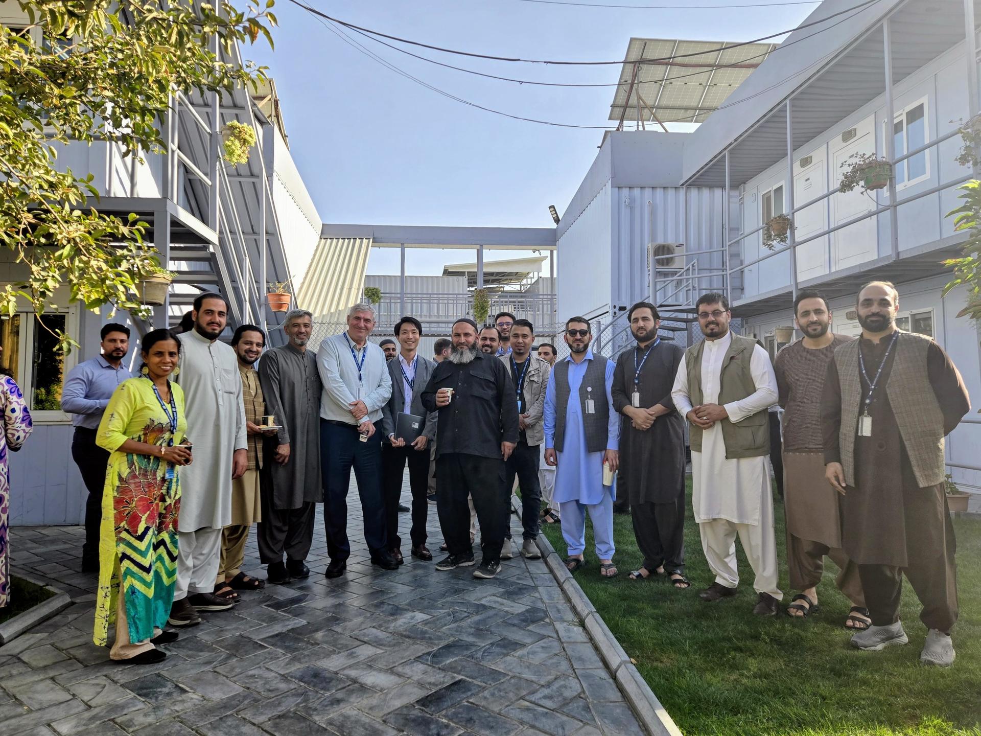 Group of diverse people in formal and traditional attire posing on a sunny street.