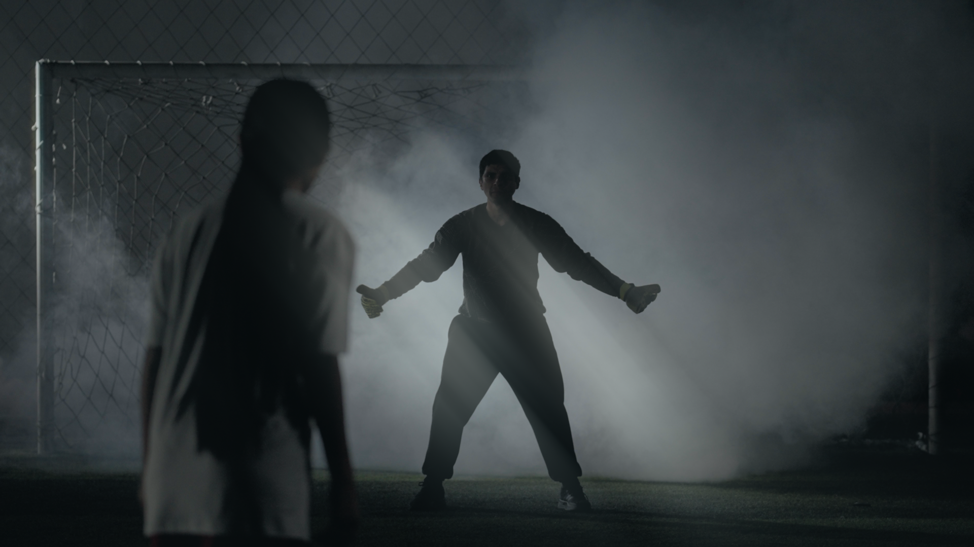 Two silhouetted figures in a smoky, blue-lit scene; one with arms outstretched.