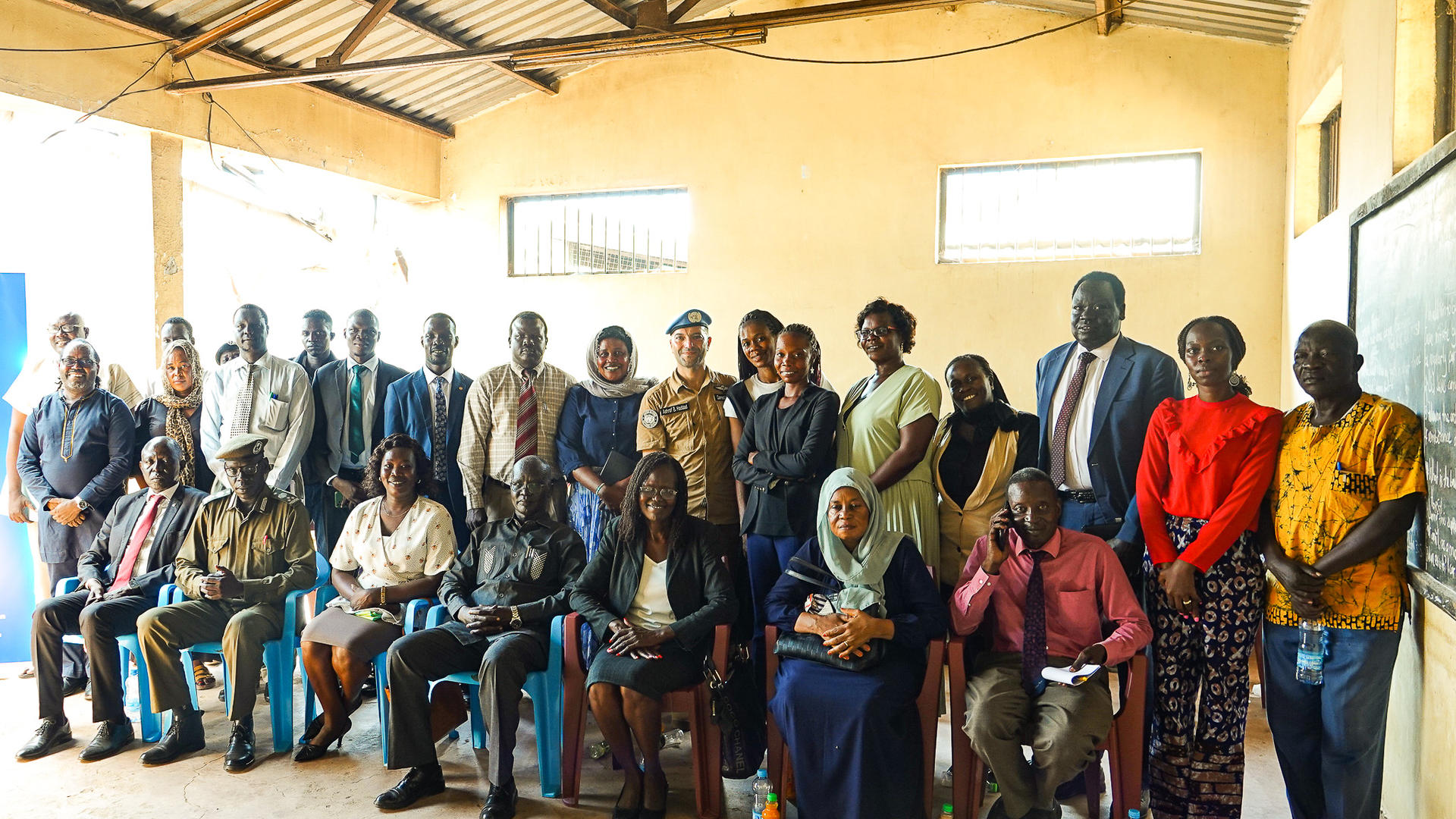 Group of diverse adults posing for a photo in a classroom; seated front, others standing.