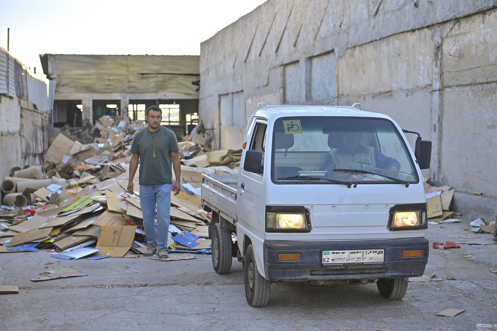 Photo: man in dark shirt stands beside a small white van in a rubble-filled construction site.
