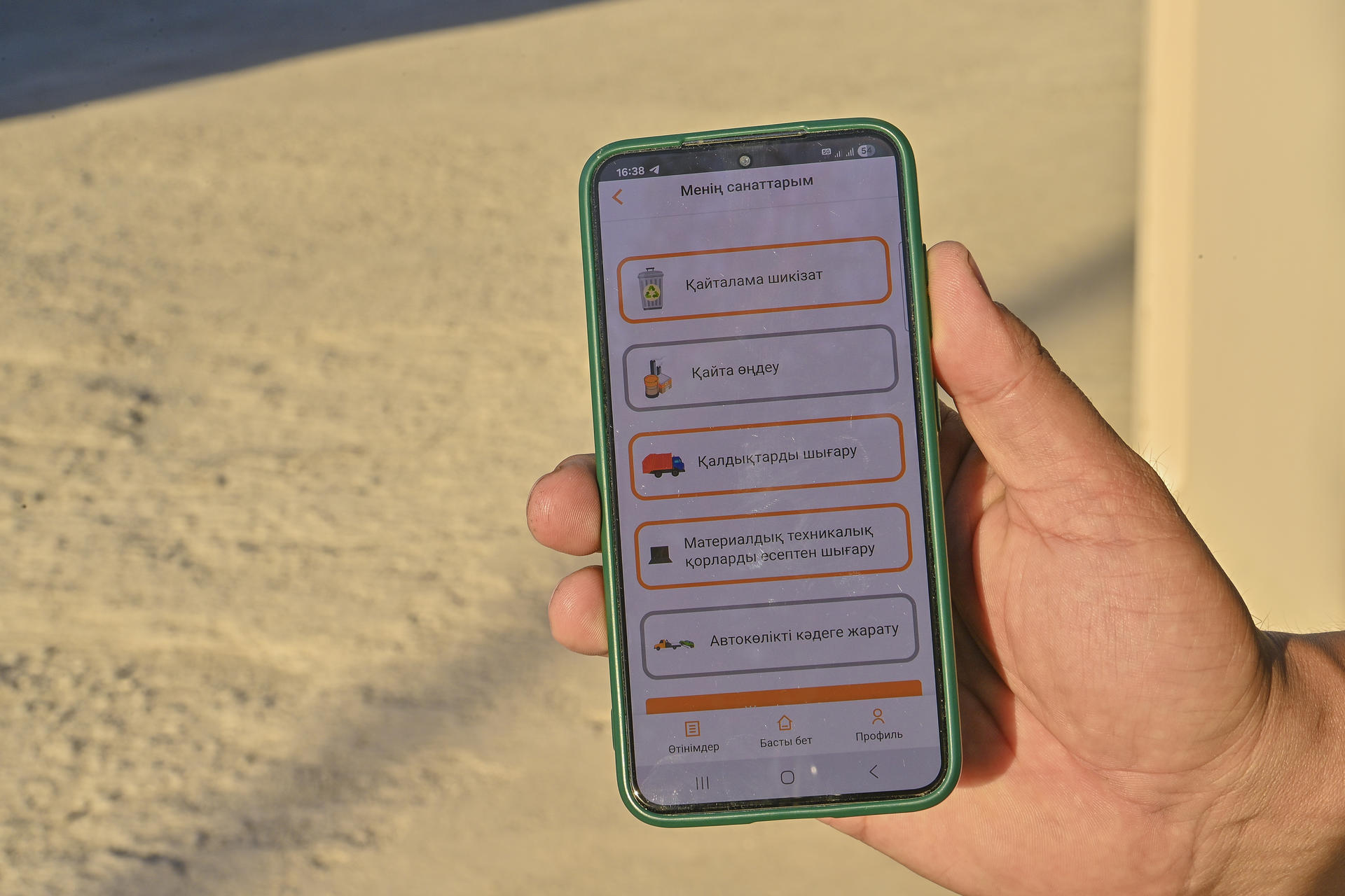 Person's hand holding a green-cased smartphone displaying a chat app on a sunny sandy beach.