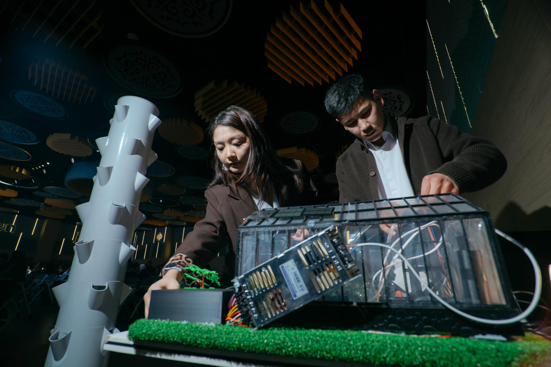 Two people examine a transparent control panel on a lab rig with a green turf surface.
