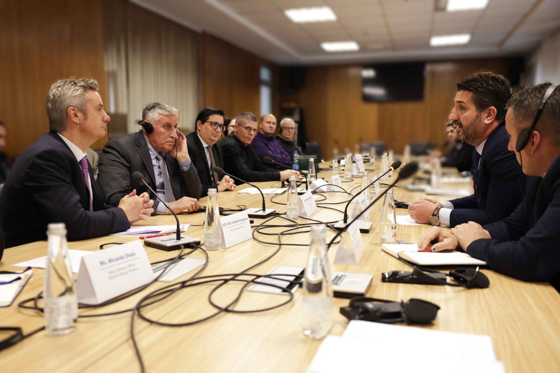 People sit around a long conference table with nameplates in a boardroom meeting.
