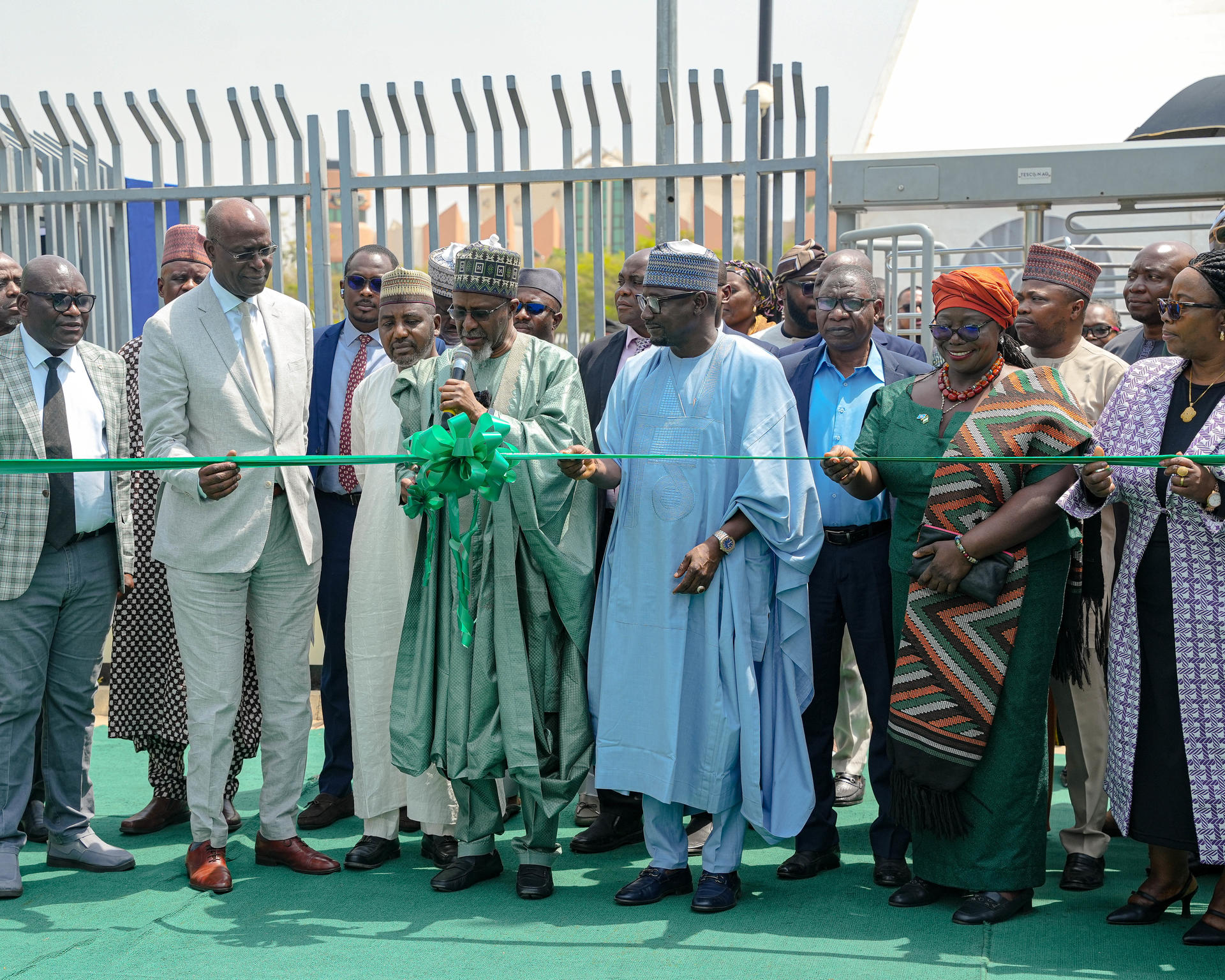 Group of dignitaries in traditional outfits at an outdoor green ribbon-cutting ceremony.