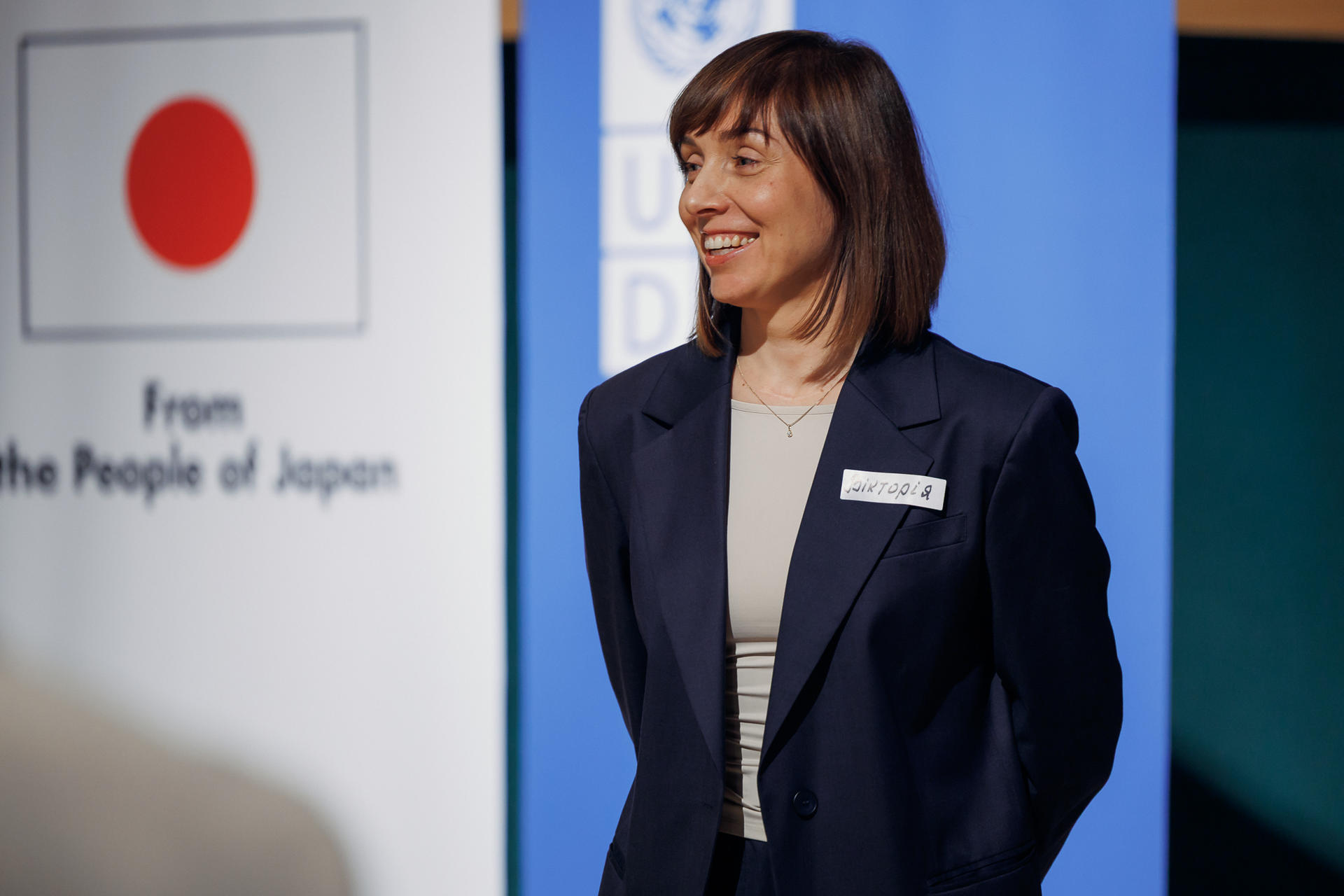Professional woman in a navy blazer with a name tag beside a Japanese flag display.
