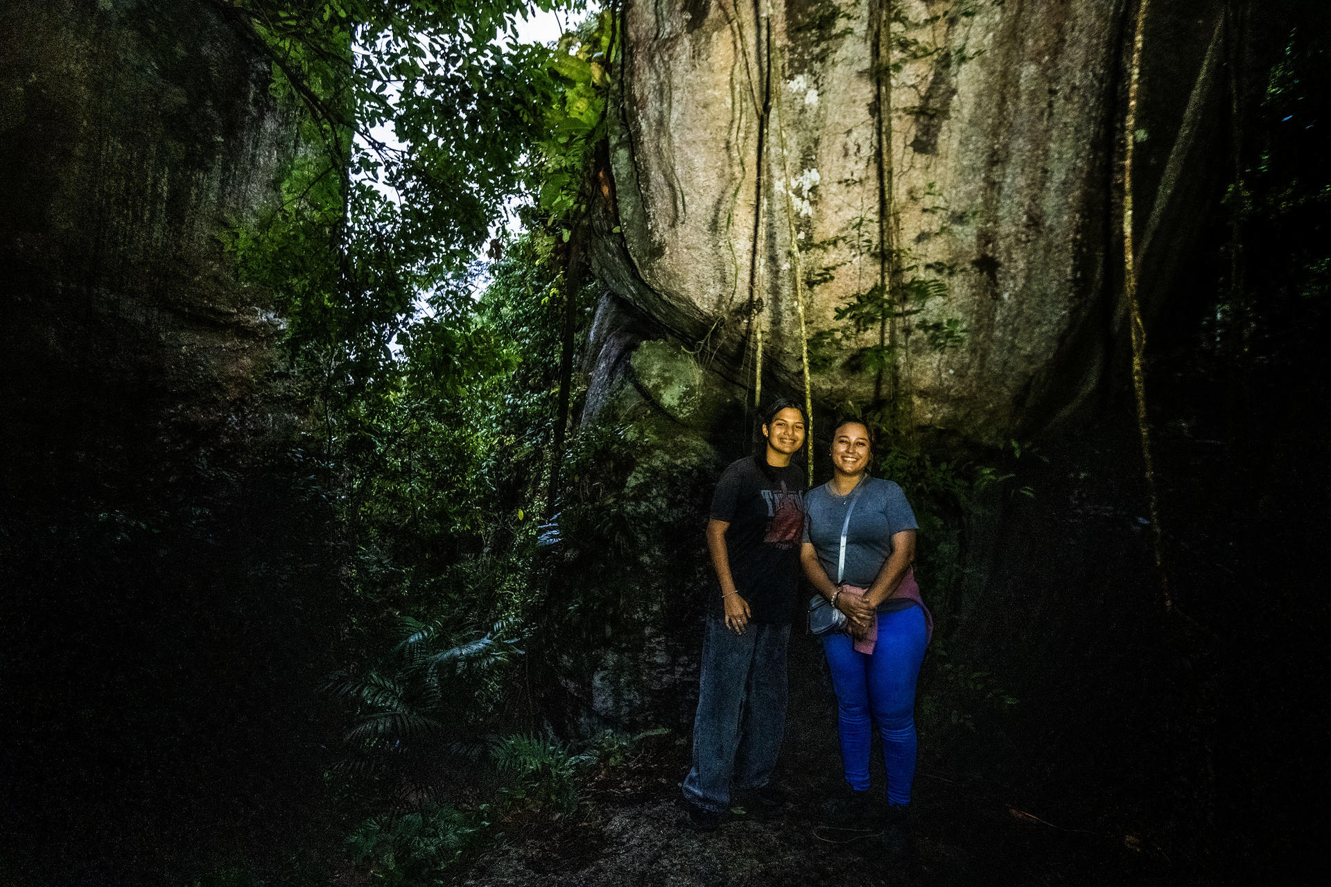 Two people stand close together in a dark forest canyon with tall mossy rock walls, smiling.