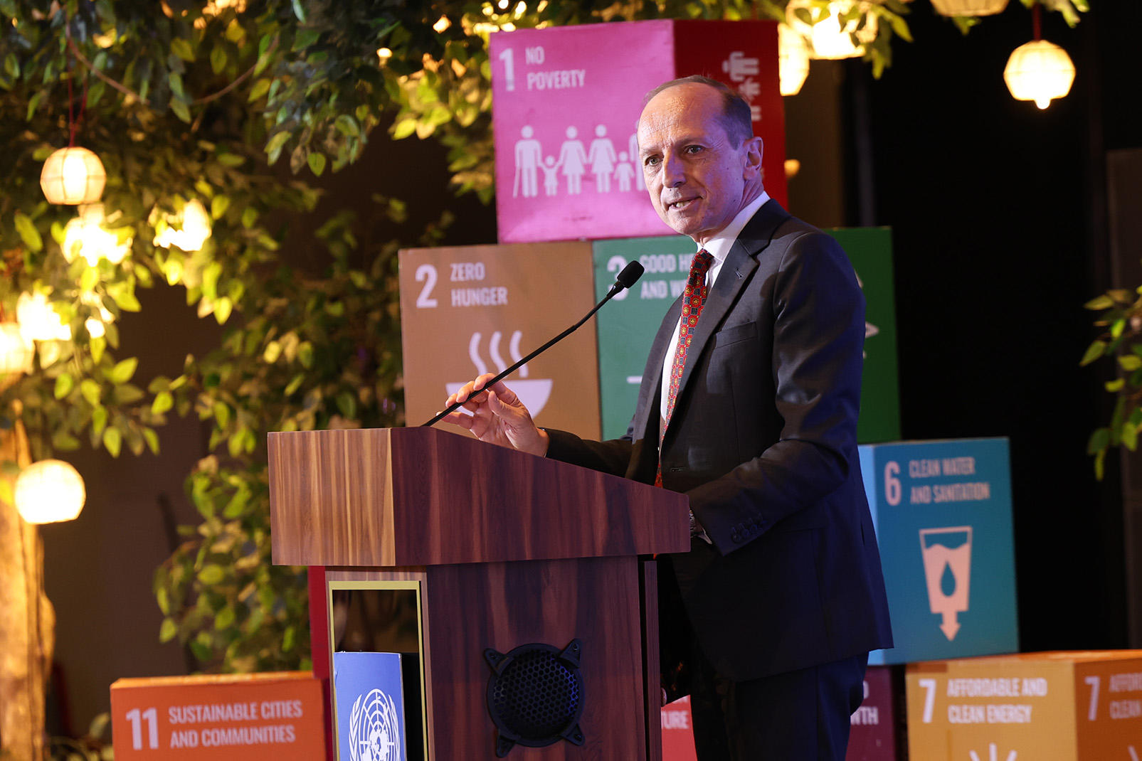 Photograph of a man in a suit speaking at a podium with SDG banners in the background.