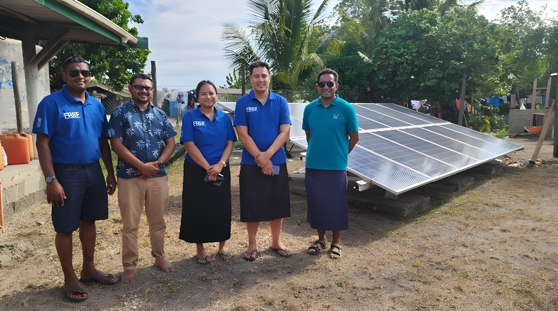 Group of people in blue shirts standing outdoors beside solar panels in a rural area.