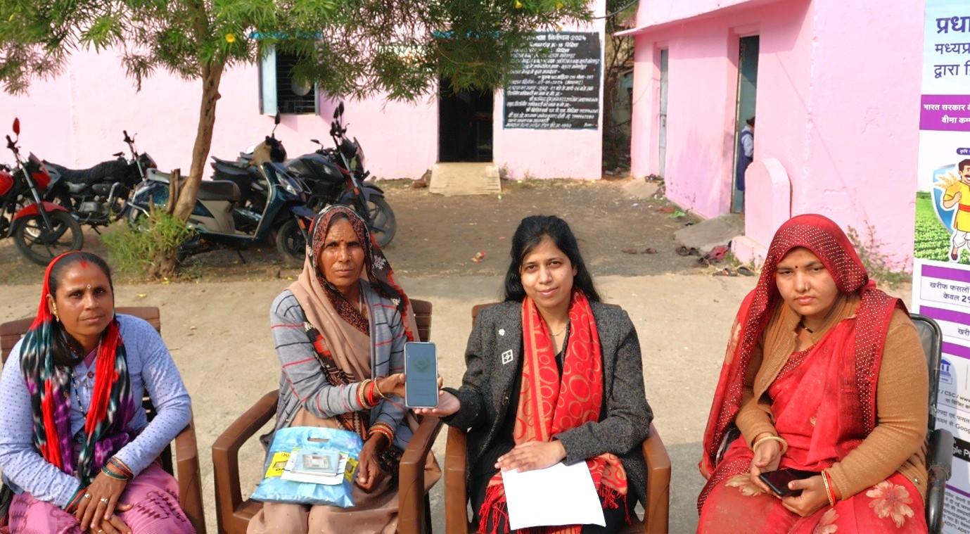 Four women sit on chairs outdoors along a pink wall, holding papers.