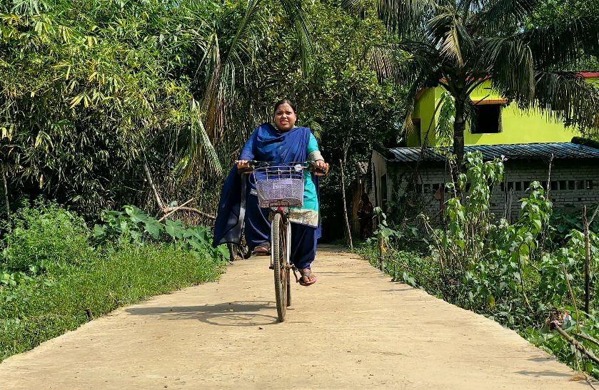 Person riding a bicycle on a sunny rural path bordered by lush greenery.