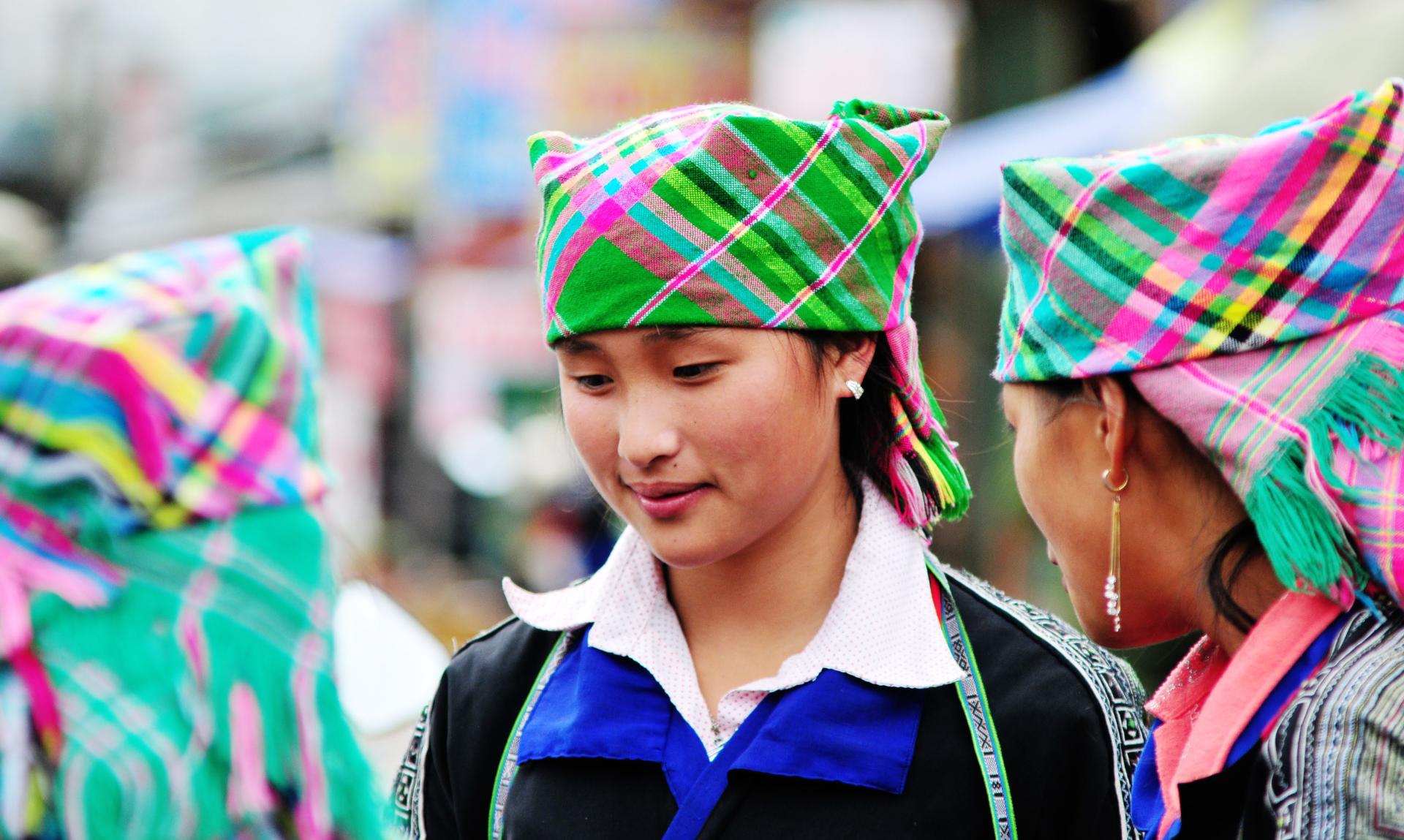 Two people in bright plaid headscarves talking outdoors; one wears a blue uniform.