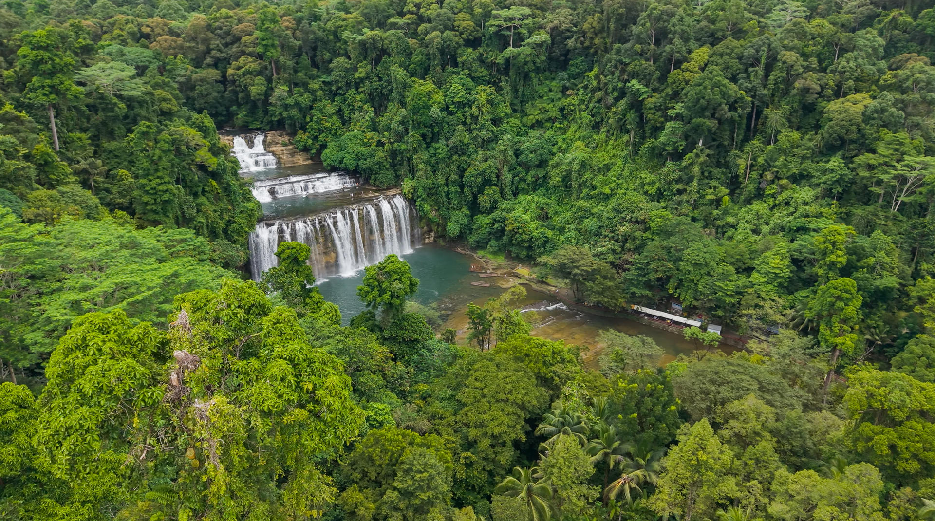 Lush rainforest surrounds a cascading multi-tiered waterfall feeding a calm pool.