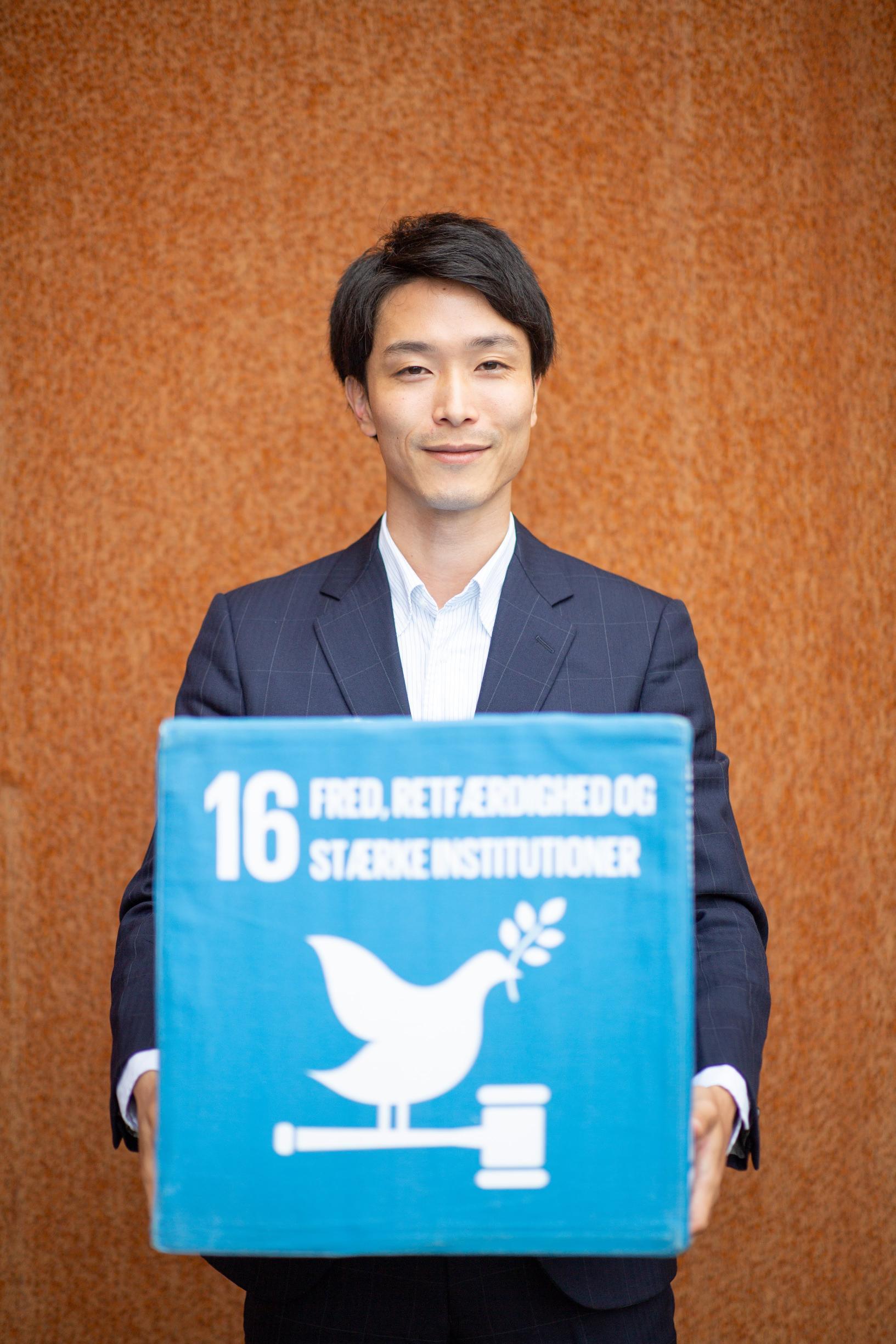 Person in a suit holding a blue box with a white dove illustration, standing against an orange wall.