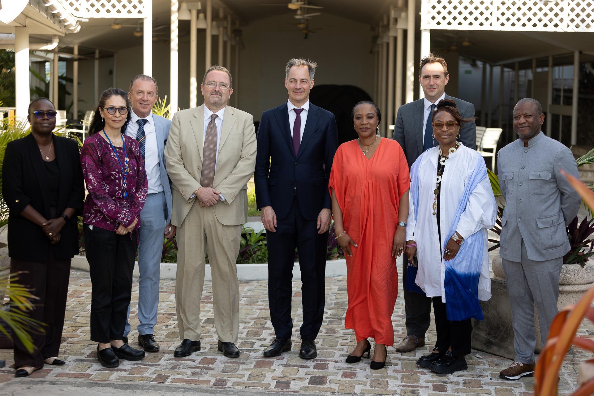 Group of people standing in a row on a tiled front porch, dressed in formal and traditional attire.