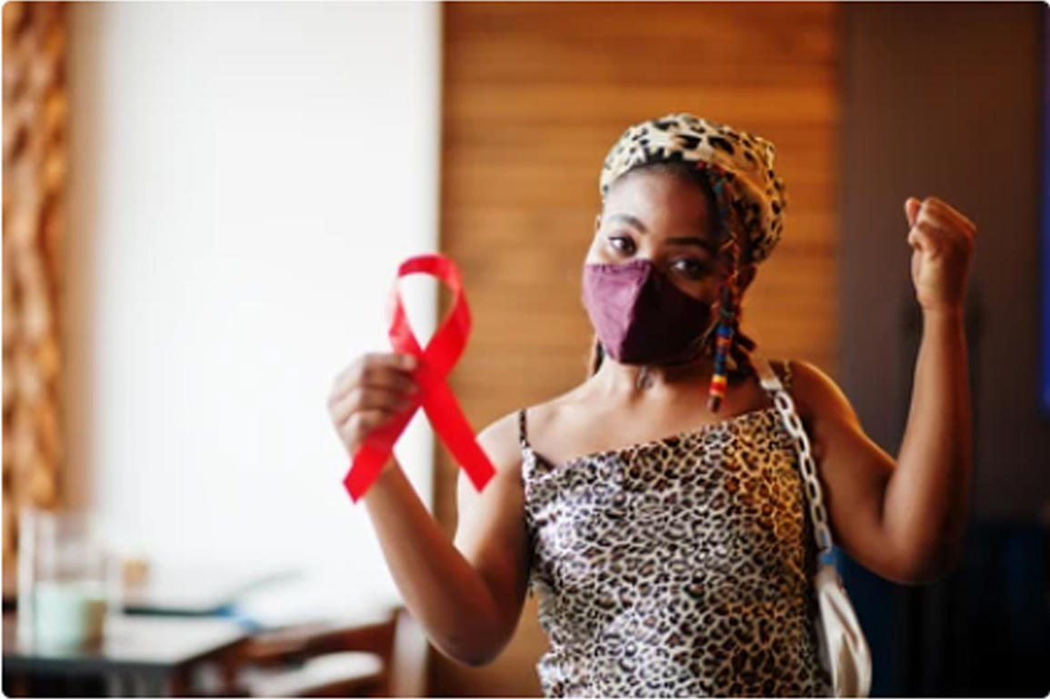 Person in leopard-print top holds a red awareness ribbon, fist raised, in a home.