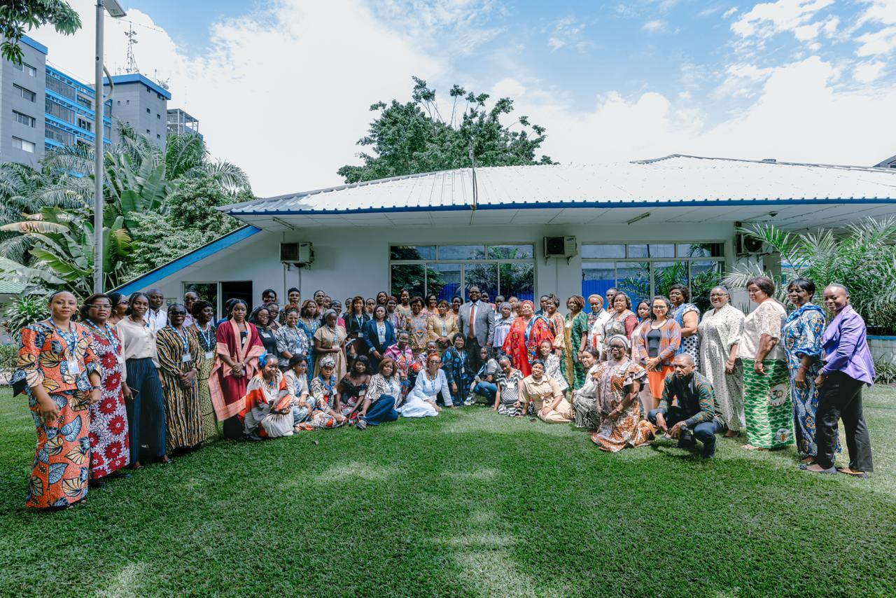 Group of people posing on a grassy lawn in front of a light-blue building.