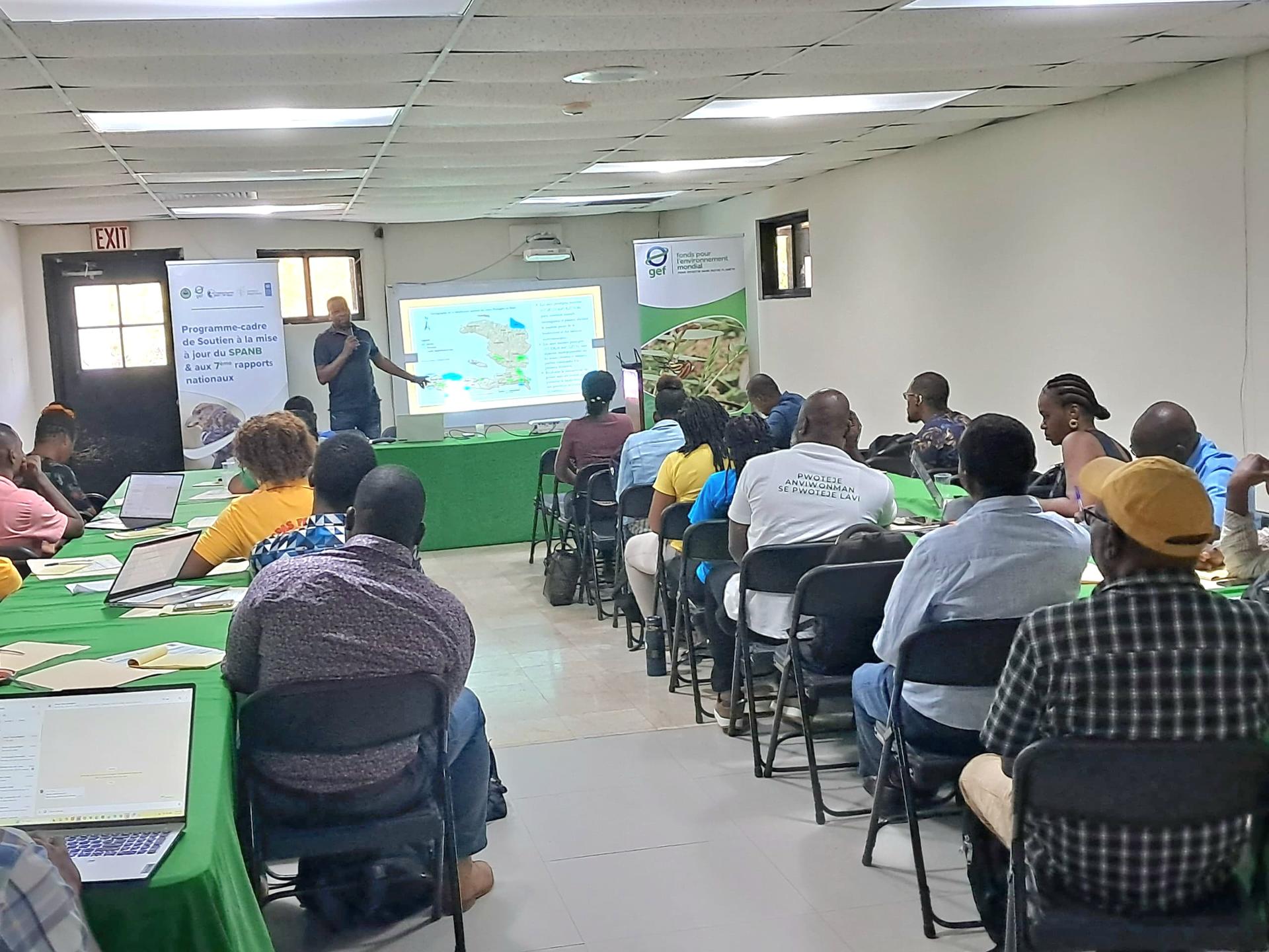 Workshop in a classroom; presenter at a podium with slides, audience seated at green-covered tables.