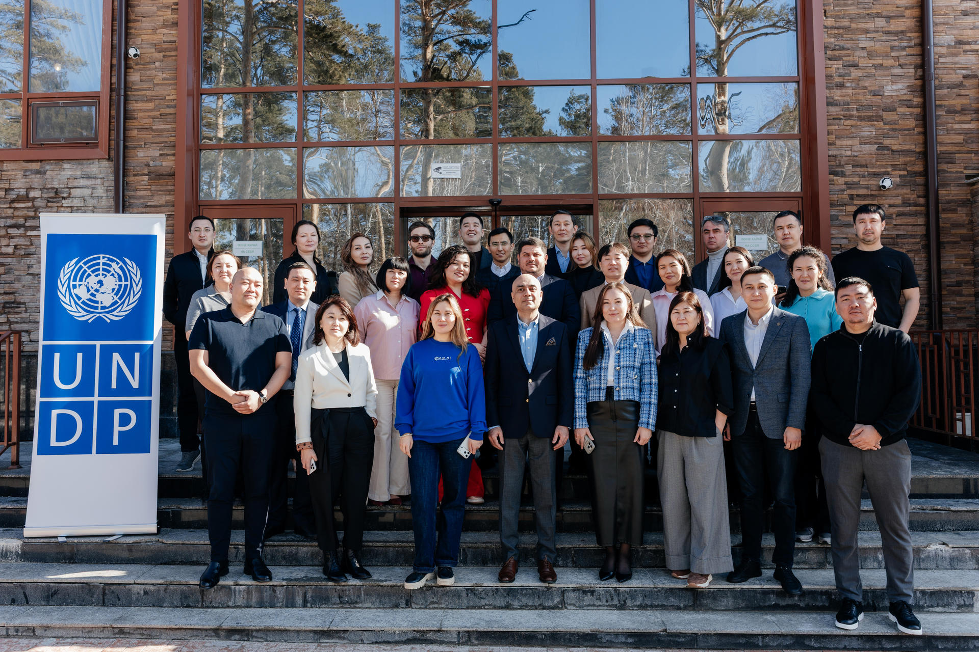 Group of diverse professionals posing on steps in front of a brick building with a UNDP banner.
