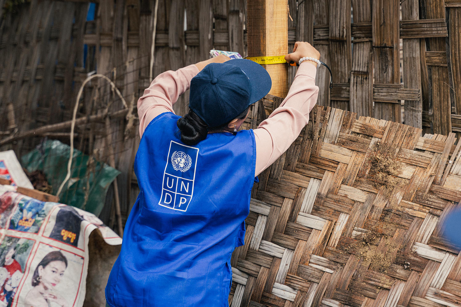 Back view of person in blue shirt with white logo, holding a woven bamboo fence.