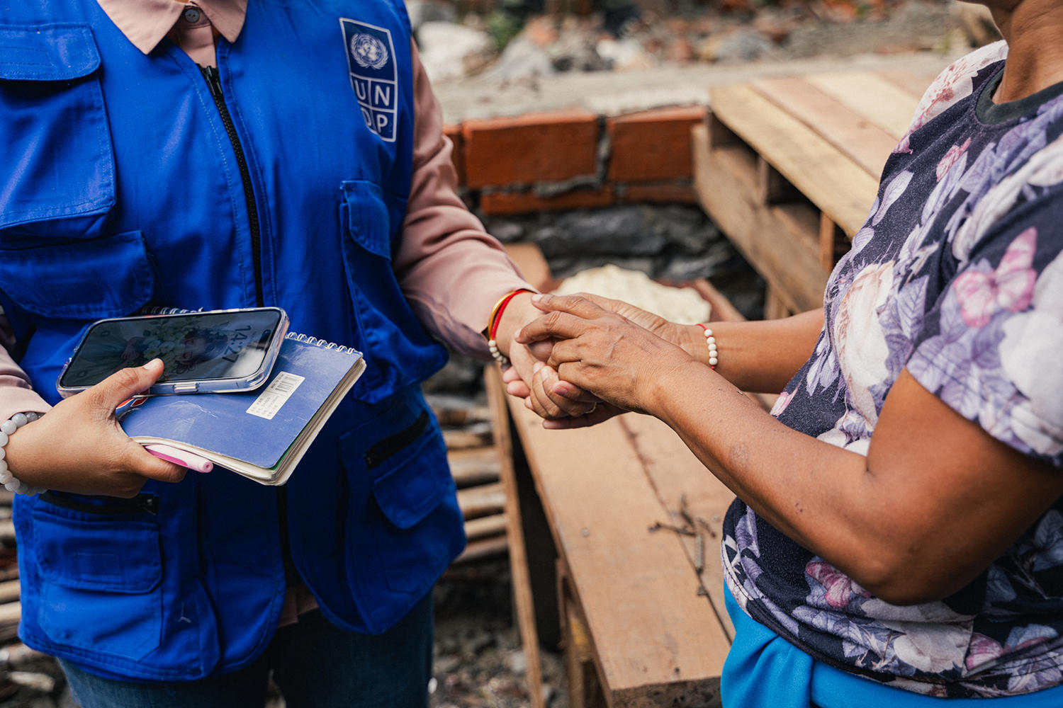 Construction site: a worker in blue uniform hands a small item to a person in a patterned shirt.