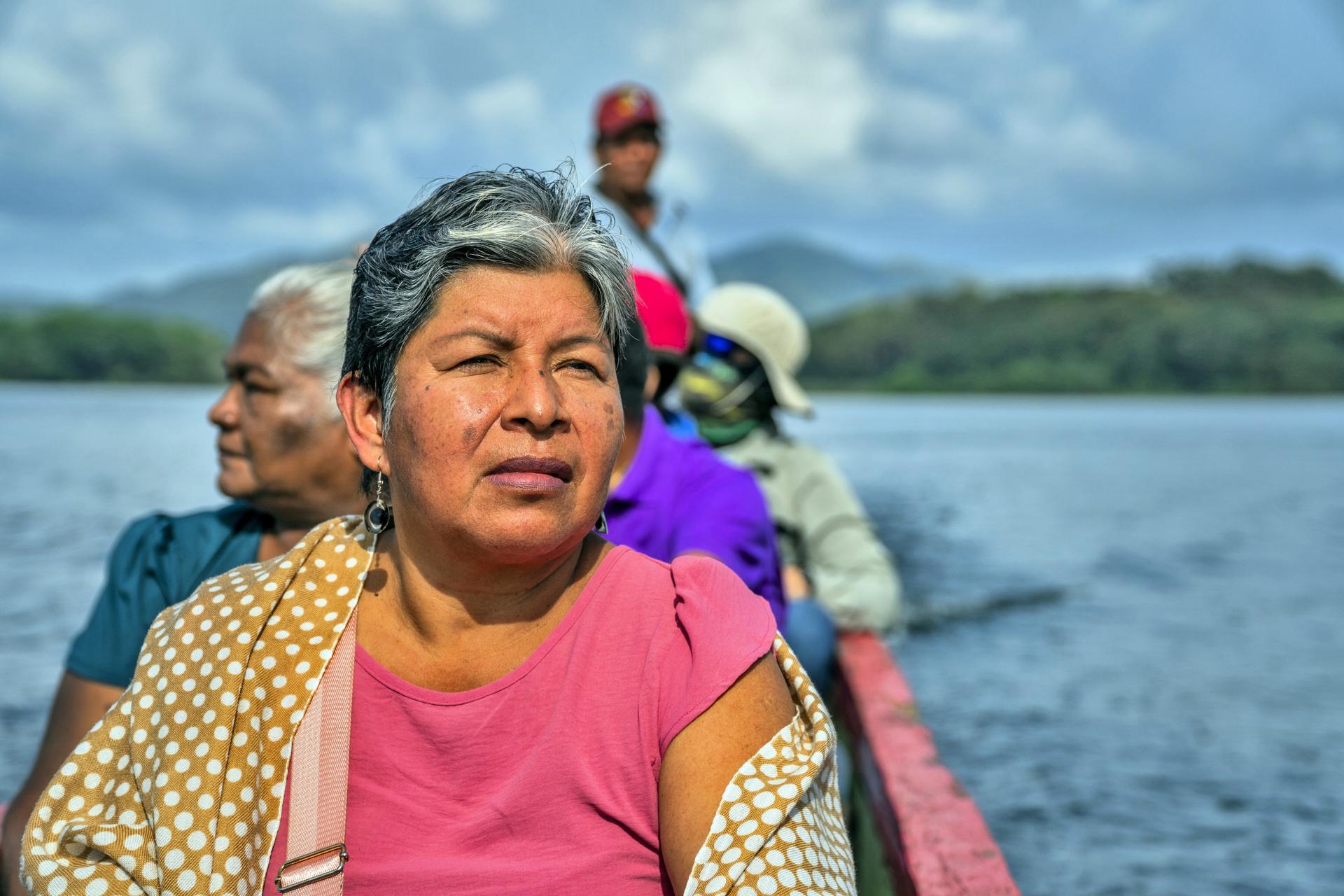 People ride a boat on calm water; foreground passenger wears pink top and yellow shawl.