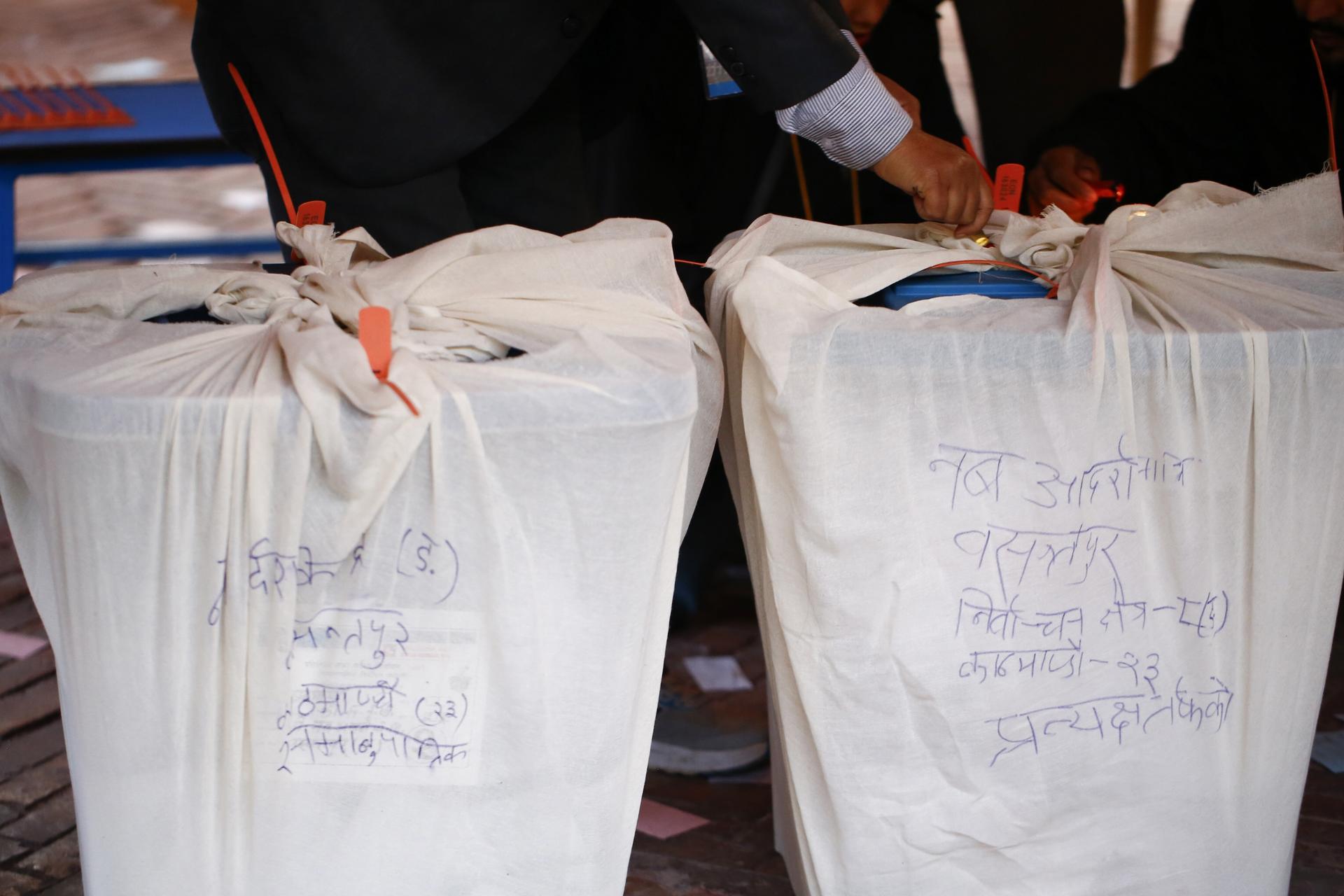 Two large white sacks tied with orange strings on a patterned red carpet, blue writing on the bags.