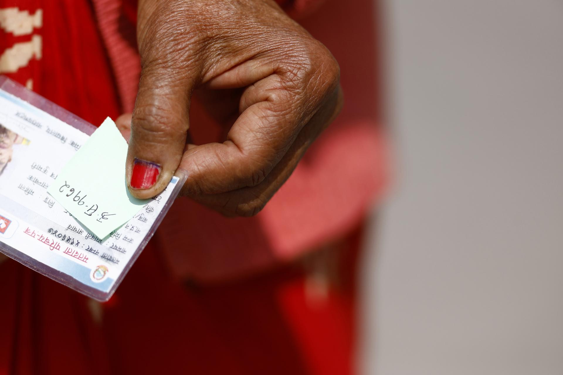 Close-up photograph of a hand with red nail polish holding a banknote.