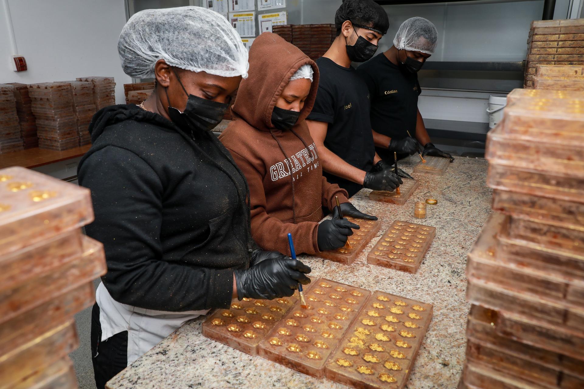 Trabajadores de una panadería, con redes para el cabello y guantes decoran chocolates en bandejas sobre una mesa de producción