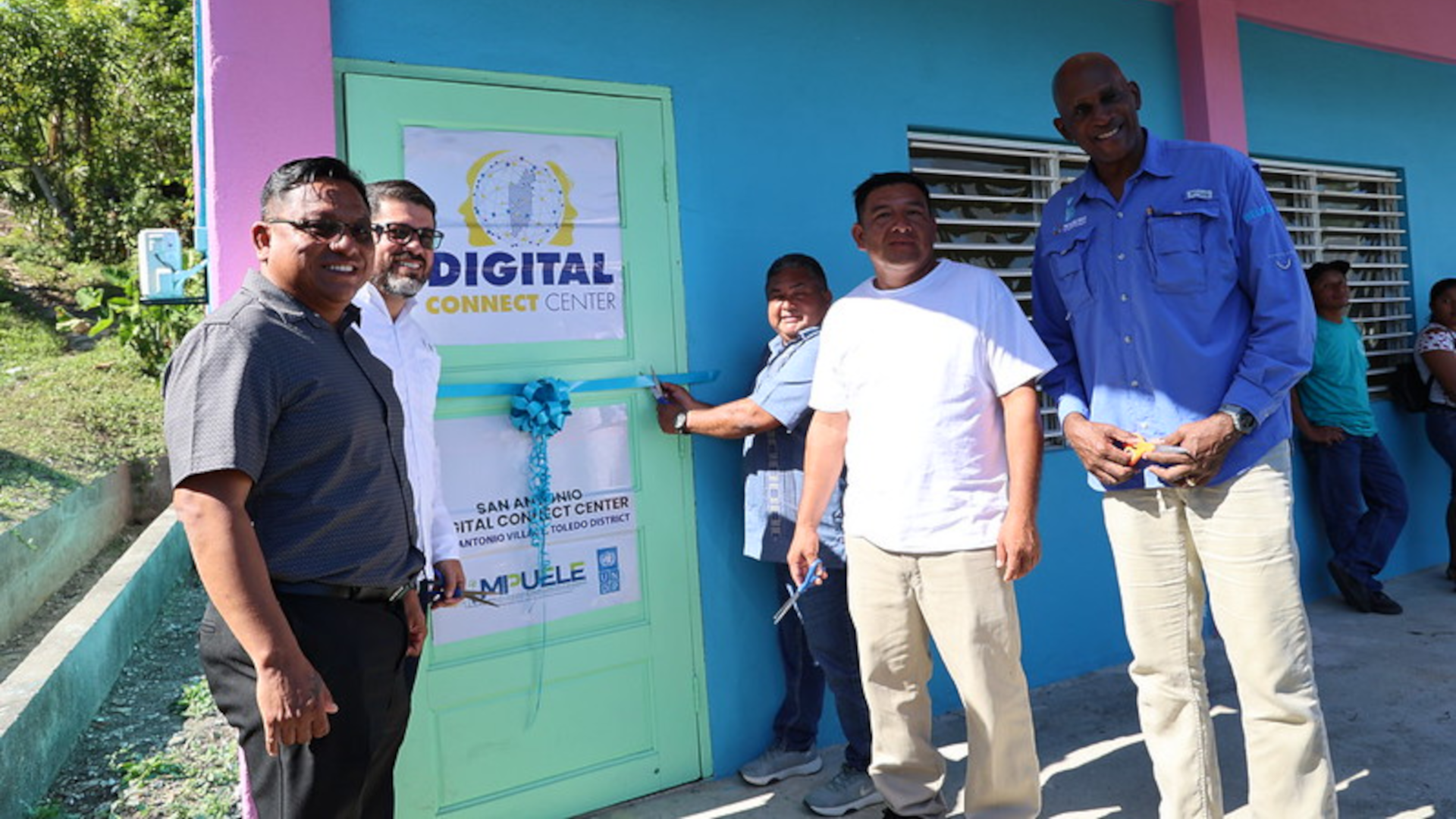 Photograph of several men standing by a teal door with a Digital Center banner in a blue building.