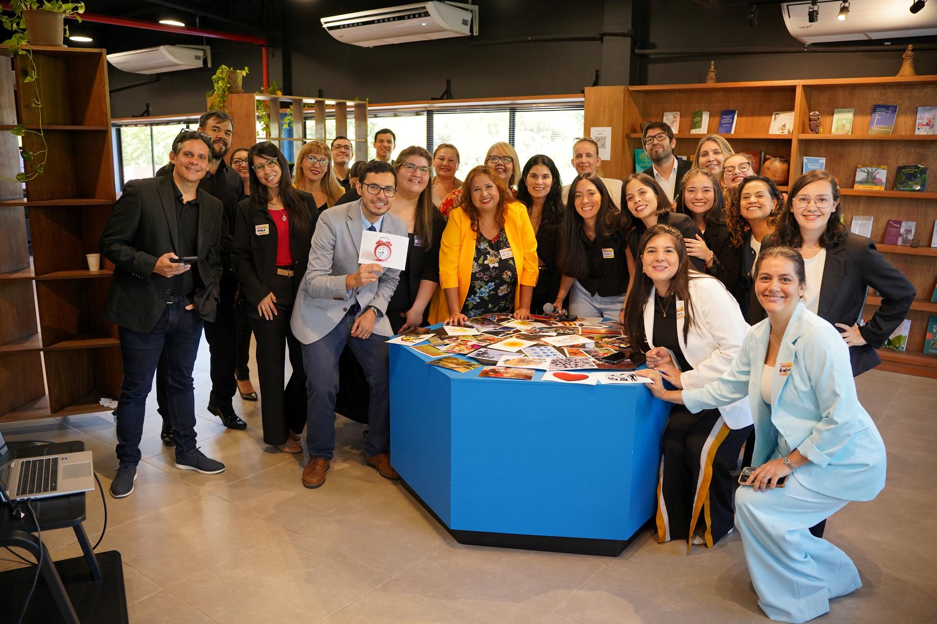Diverse group around a blue hexagonal table piled with books in a library.