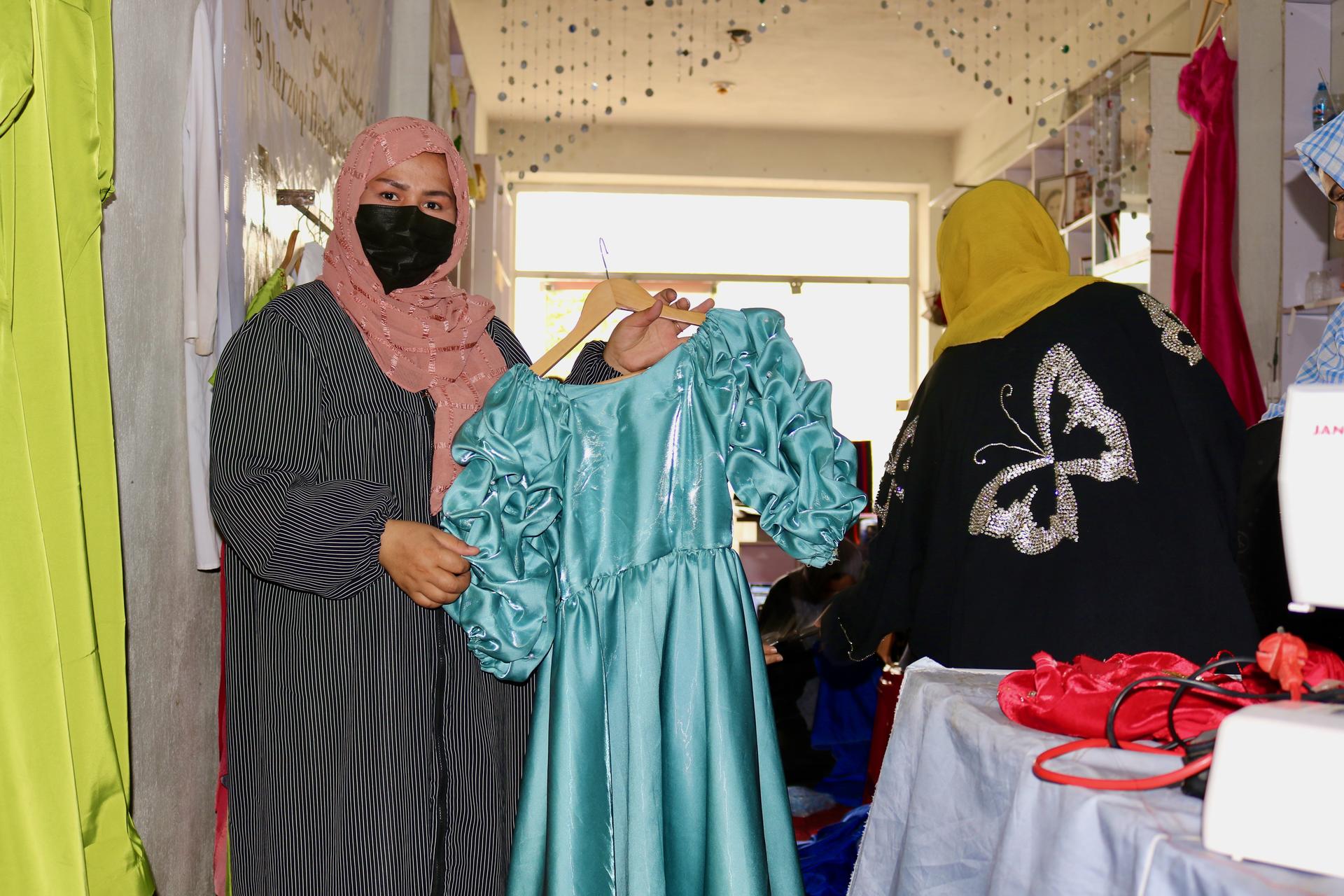 Two people in a costume shop presenting a turquoise satin gown.