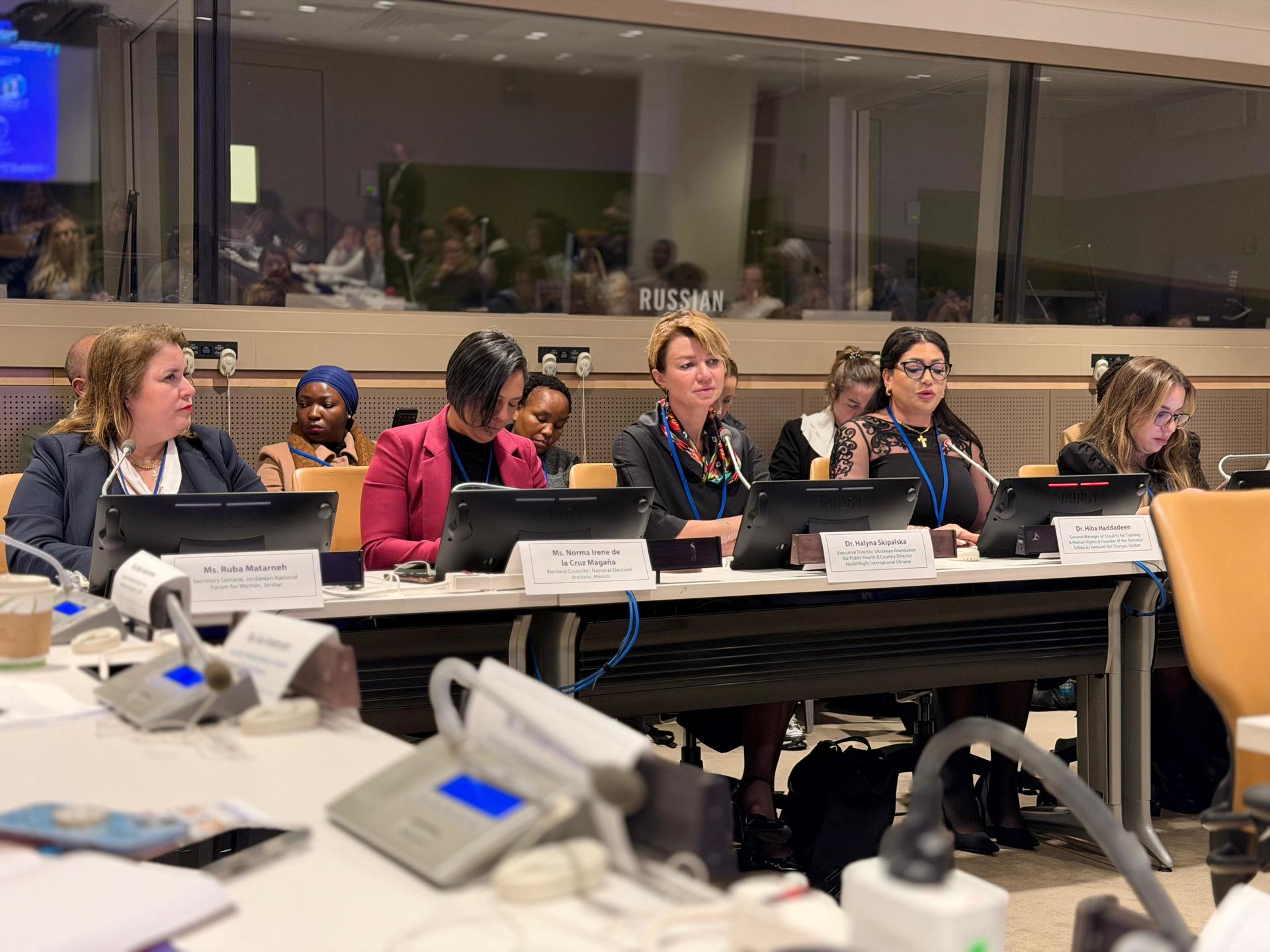 Panel of people seated at a conference table with microphones and nameplates.