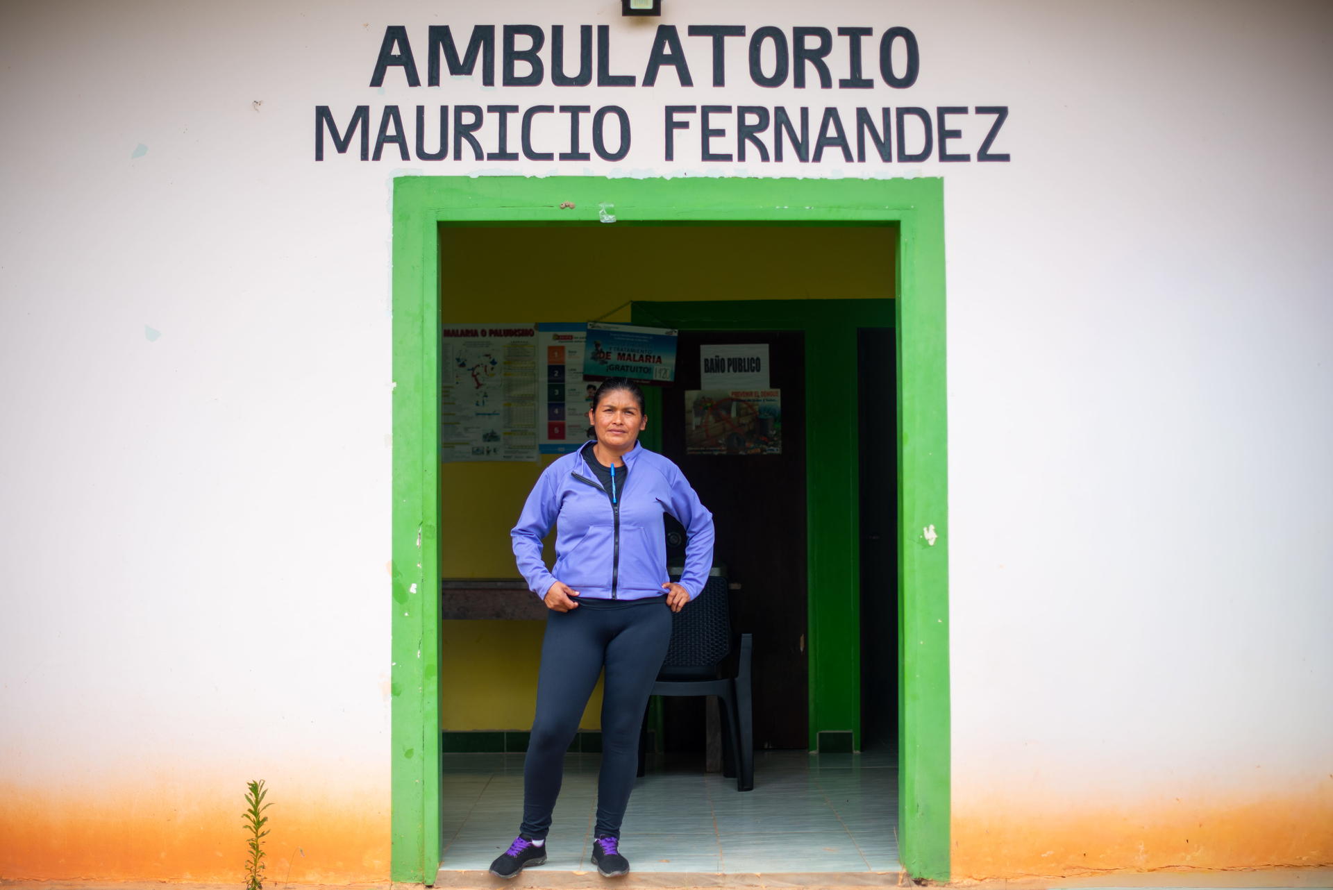 Man stands in the doorway of a clinic with a green frame; sign reads Ambulatorio Mauricio Fernandez.