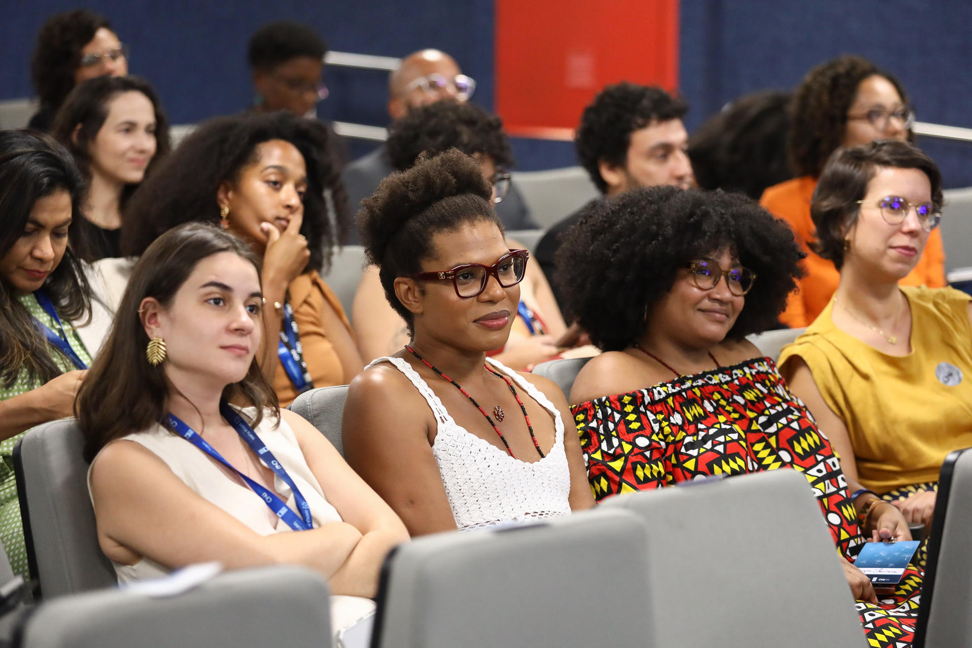 Diverse audience seated in rows at a conference, wearing lanyards.