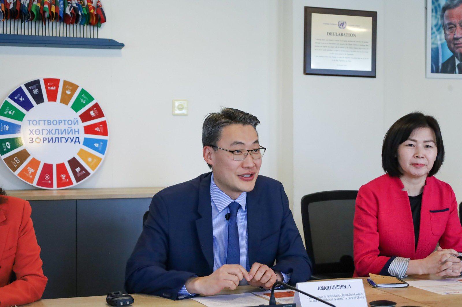Three people at a conference table in a meeting room; colorful color wheel on the wall.