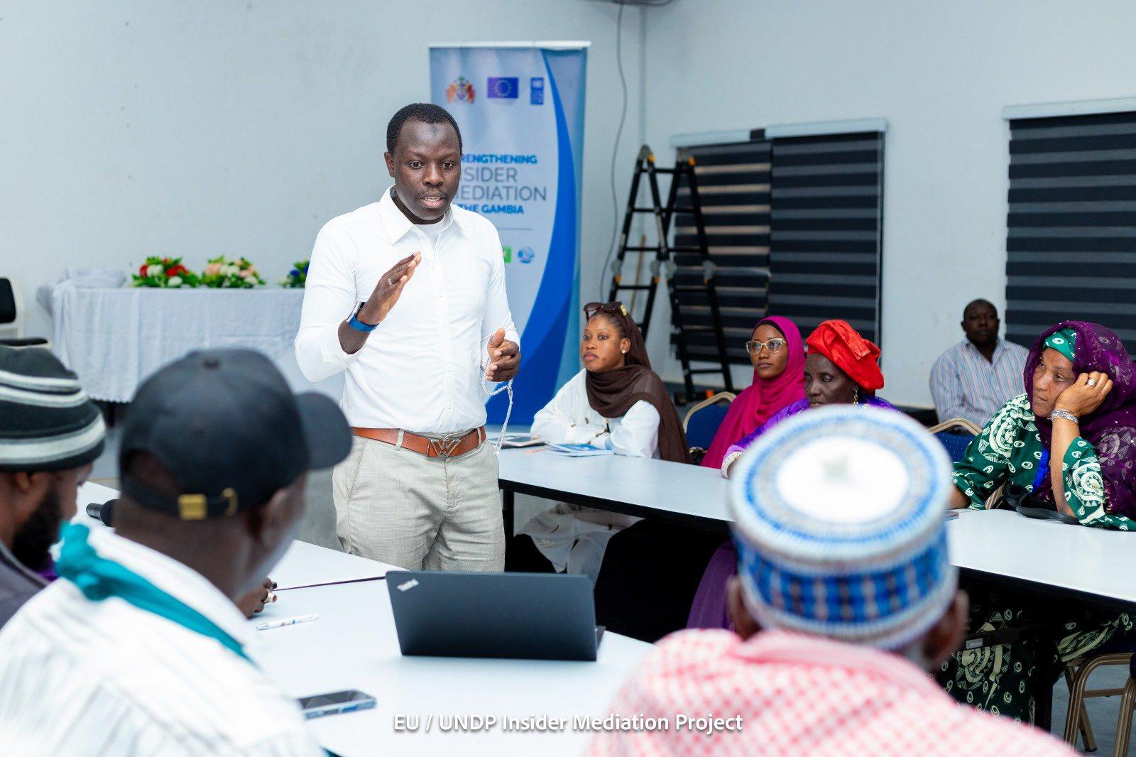 Photograph of a man in a beige shirt presenting to a diverse group at a workshop.