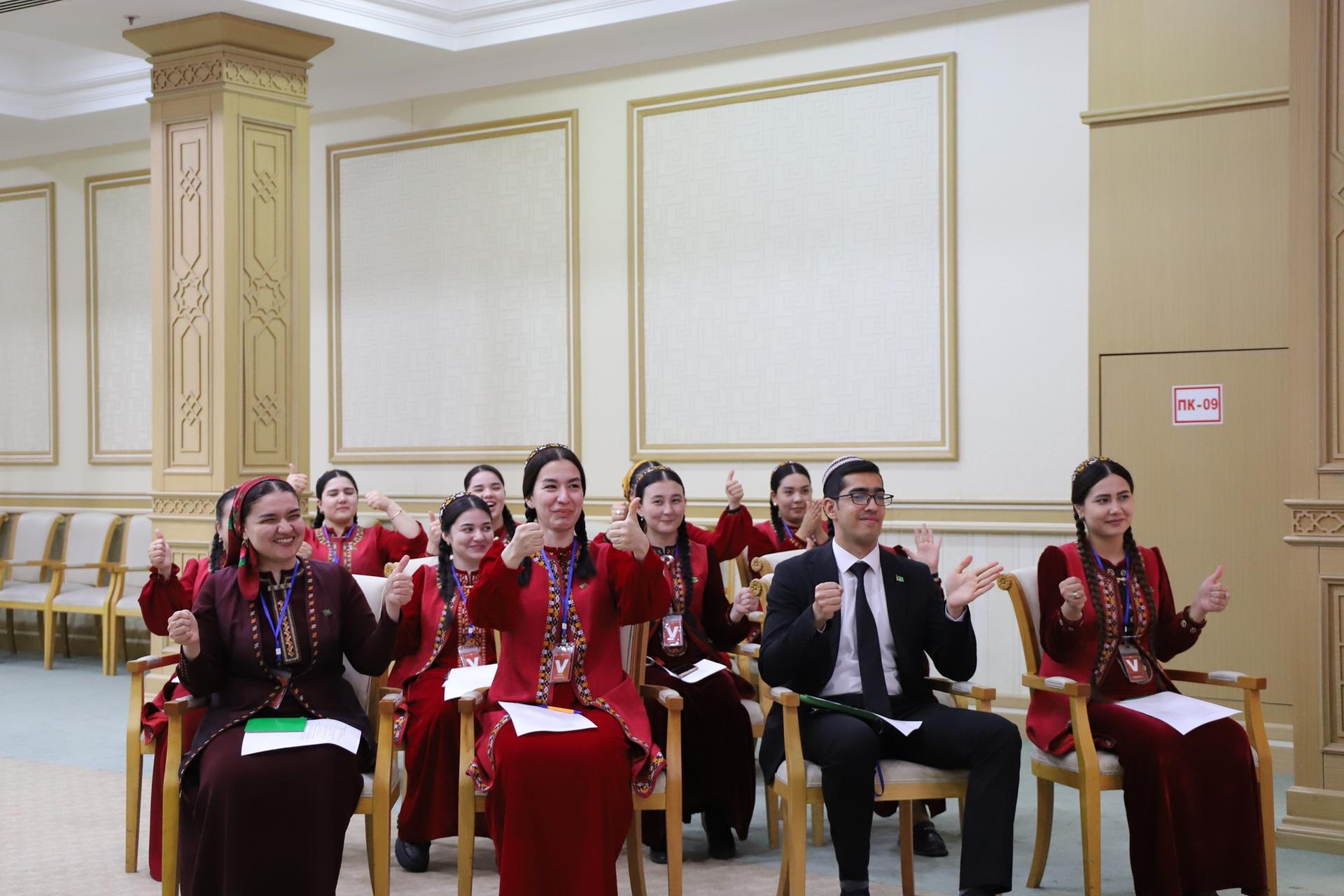 Group of people in red outfits seated in a gold-trimmed formal hall.