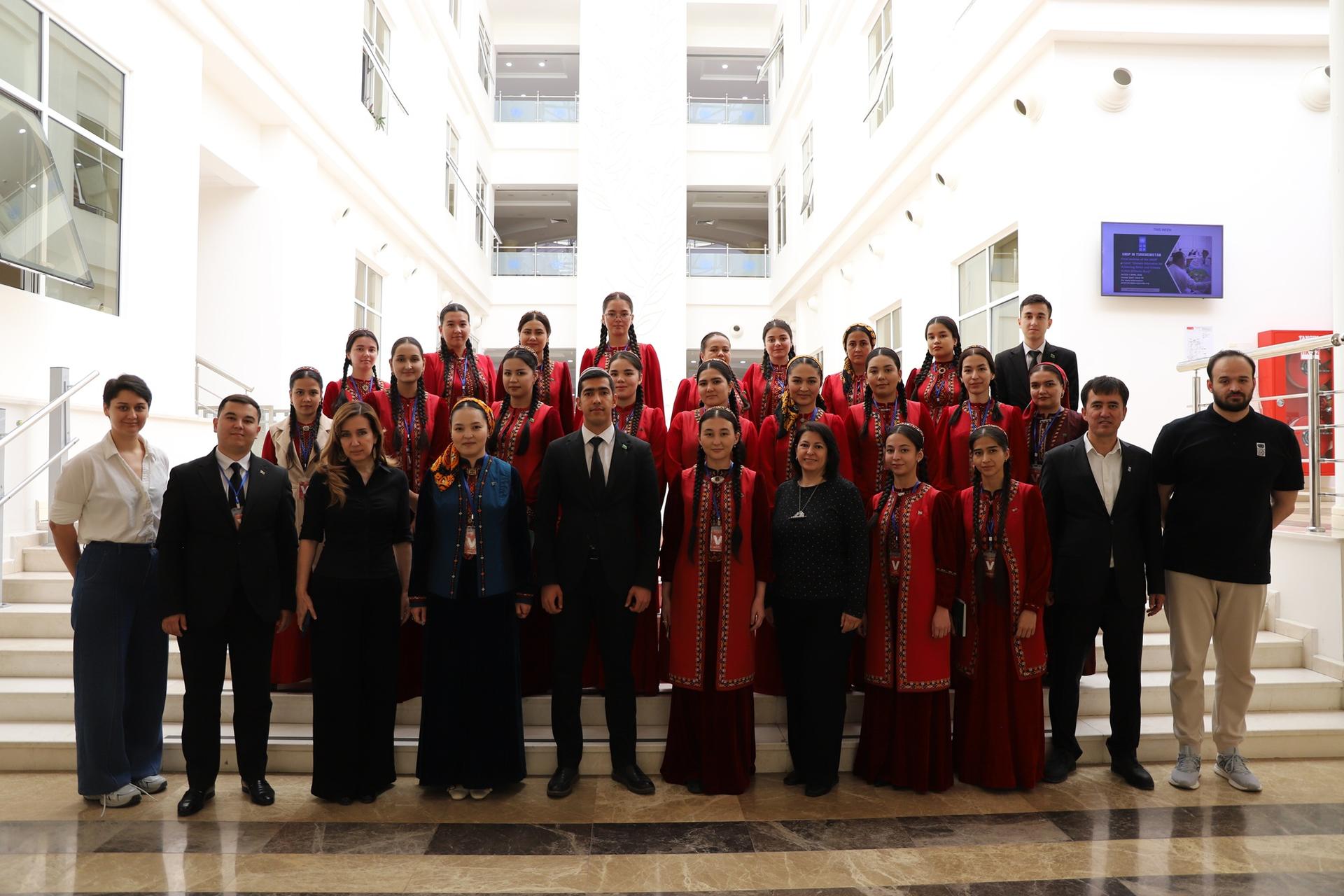 Group of people in formal attire, some in red robes, posing on a grand staircase in a bright atrium.