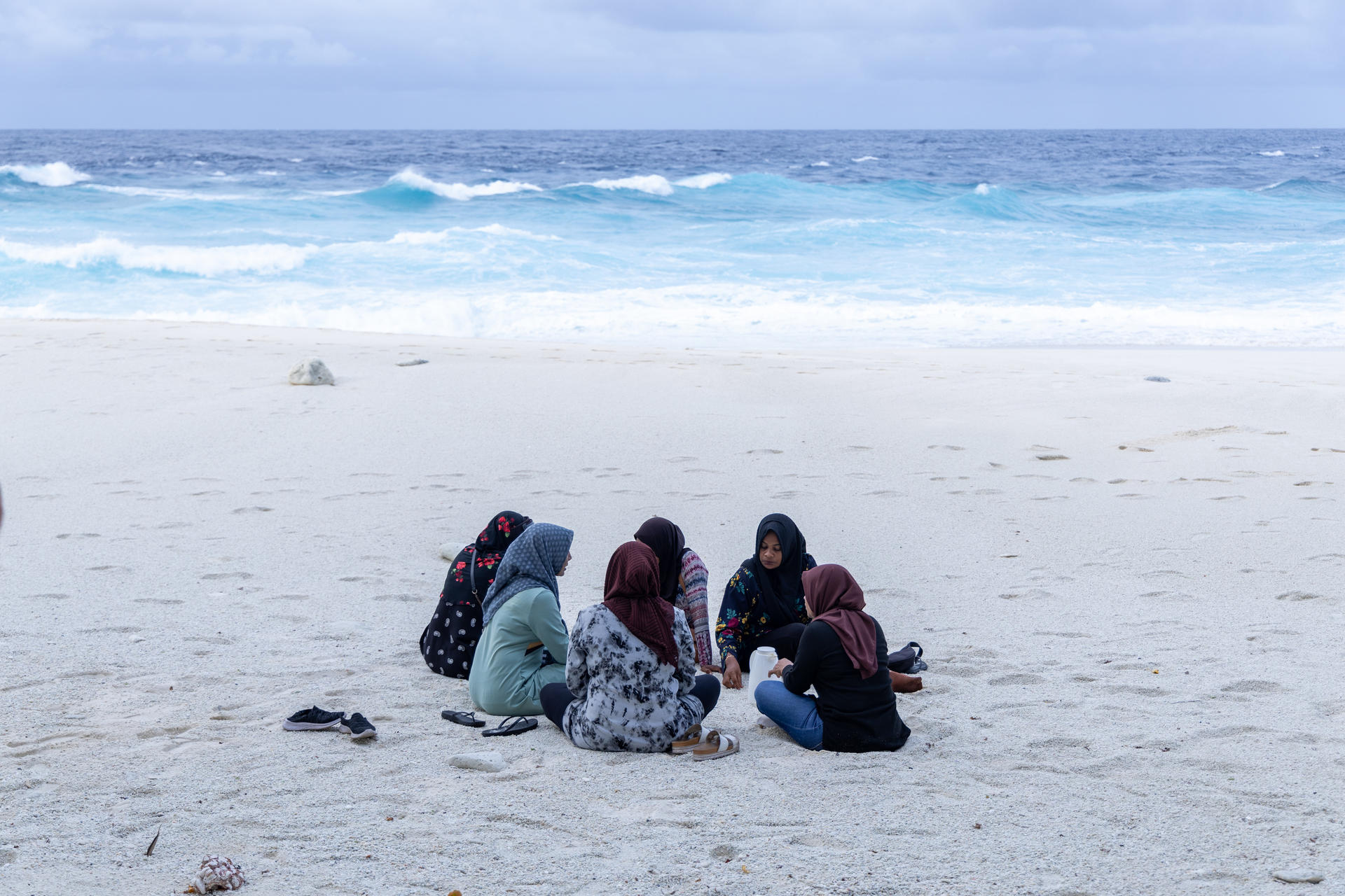 Small group of people sitting on a white-sand beach near the blue ocean.