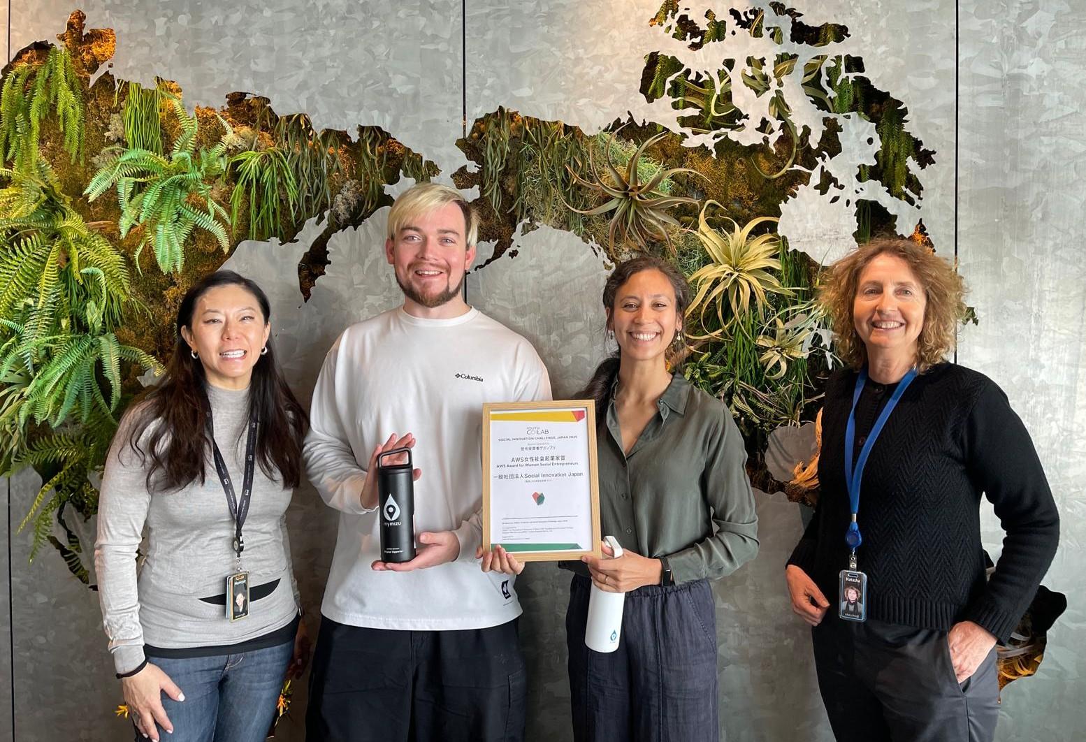 Photo of five people indoors, smiling; center holds certificate and trophy.