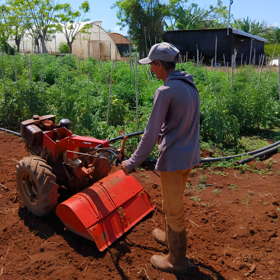 Photograph of a man operating a small red tractor with front loader on a dirt field.