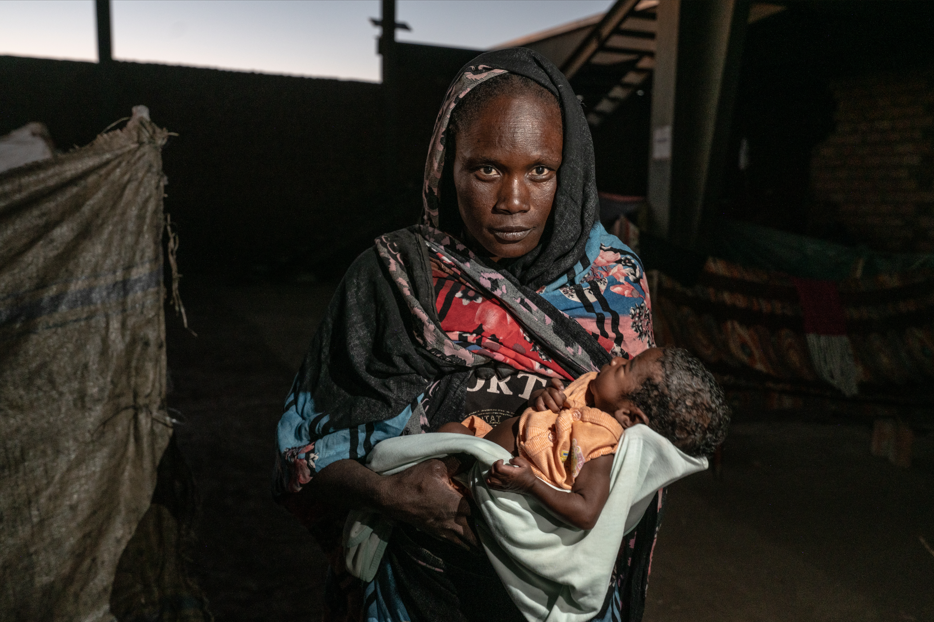 Mother in colorful attire cradles a newborn baby inside a camp
